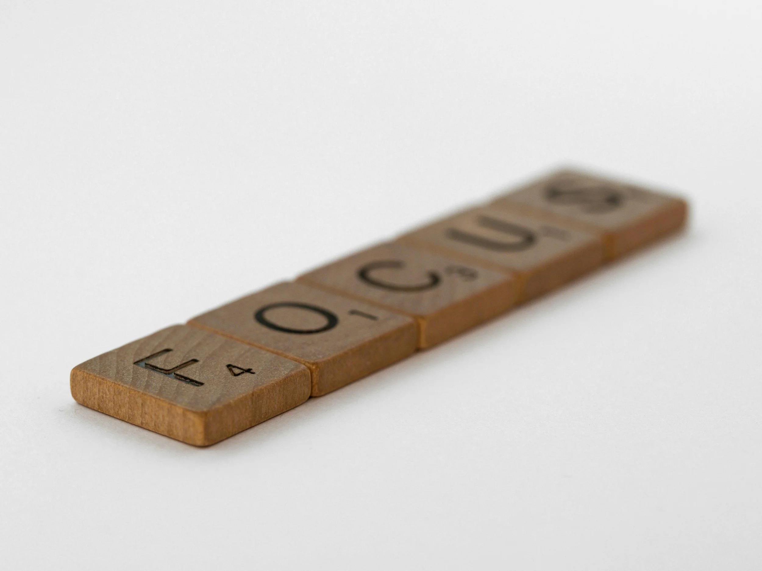 Stacked wooden Scrabble tiles spelling 'FOOD' on a white background.