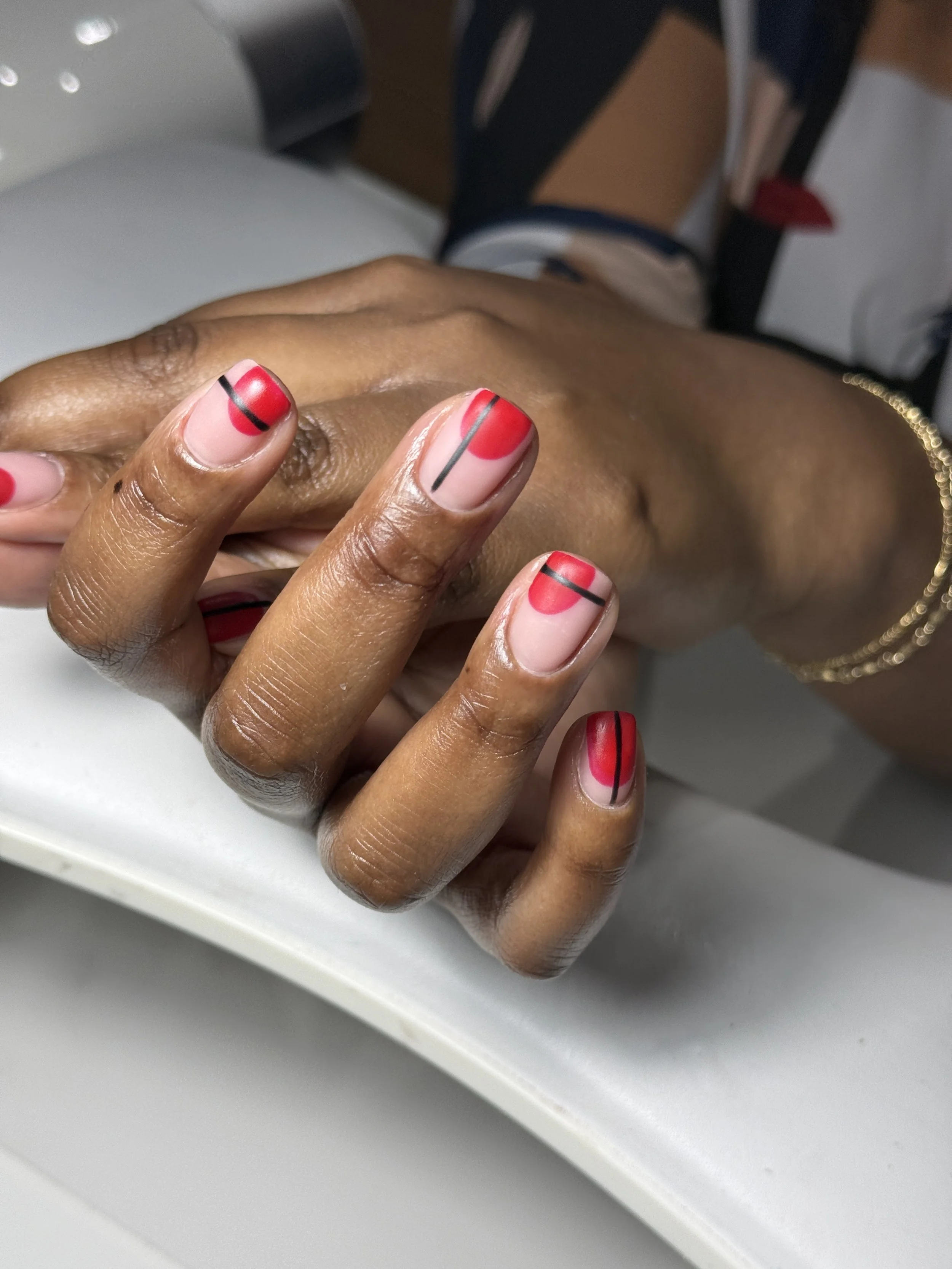 Close-up of a person's hand with freshly painted red and nude nails with black lines, resting on a flat surface.