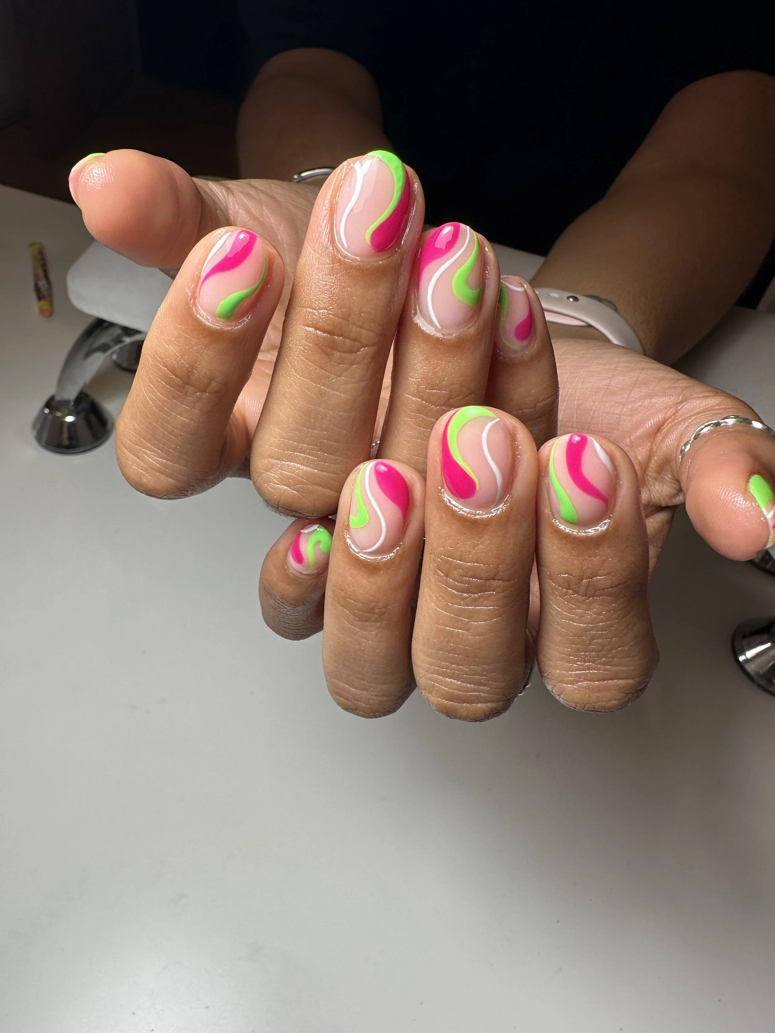 Close-up of hands with vibrant, colorful nail art featuring pink, green, and white swirls.