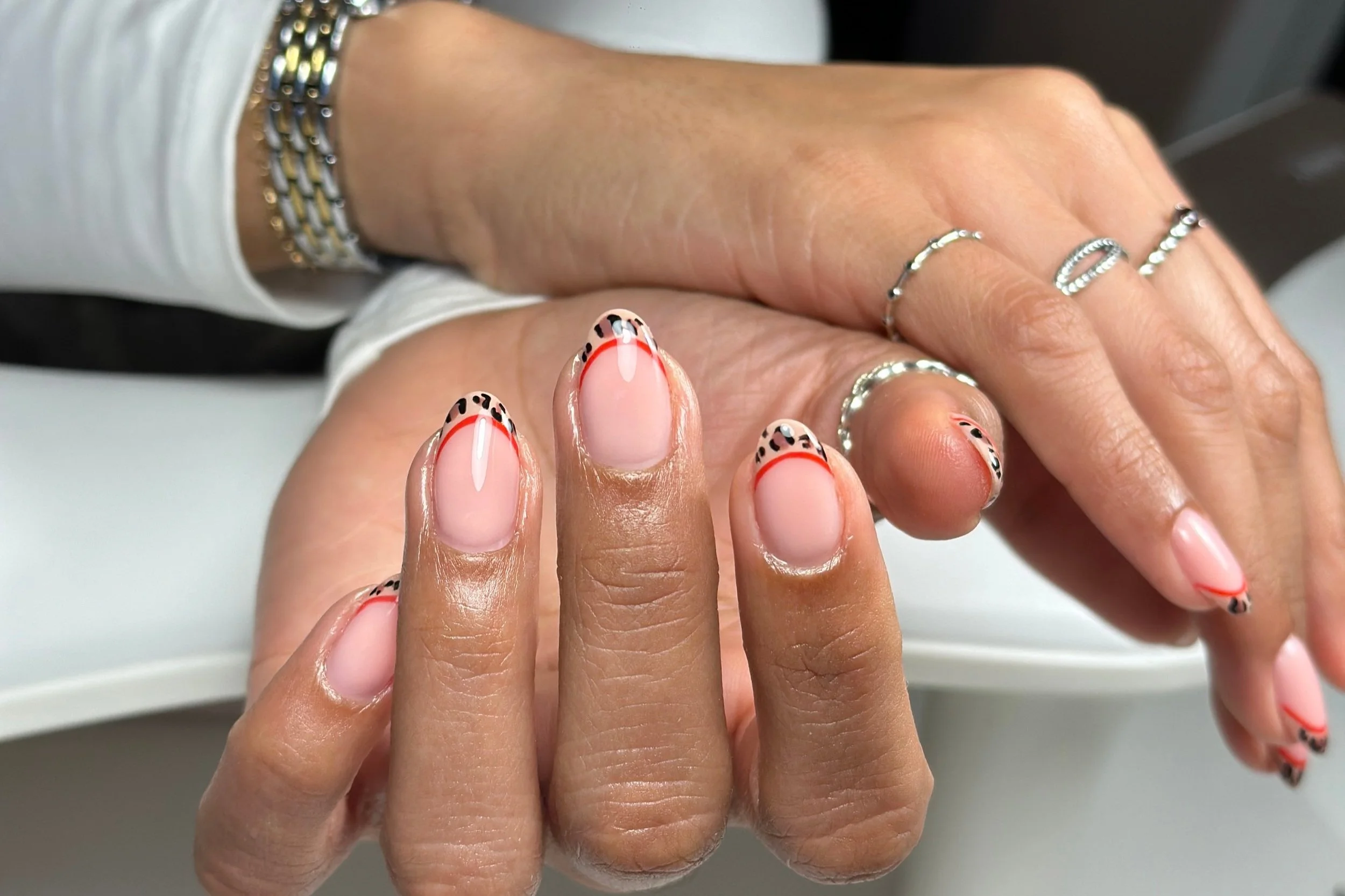 Close-up of a person’s fingers showing manicured nails with nail art, some adorned with rings, and a wrist with a bracelet.