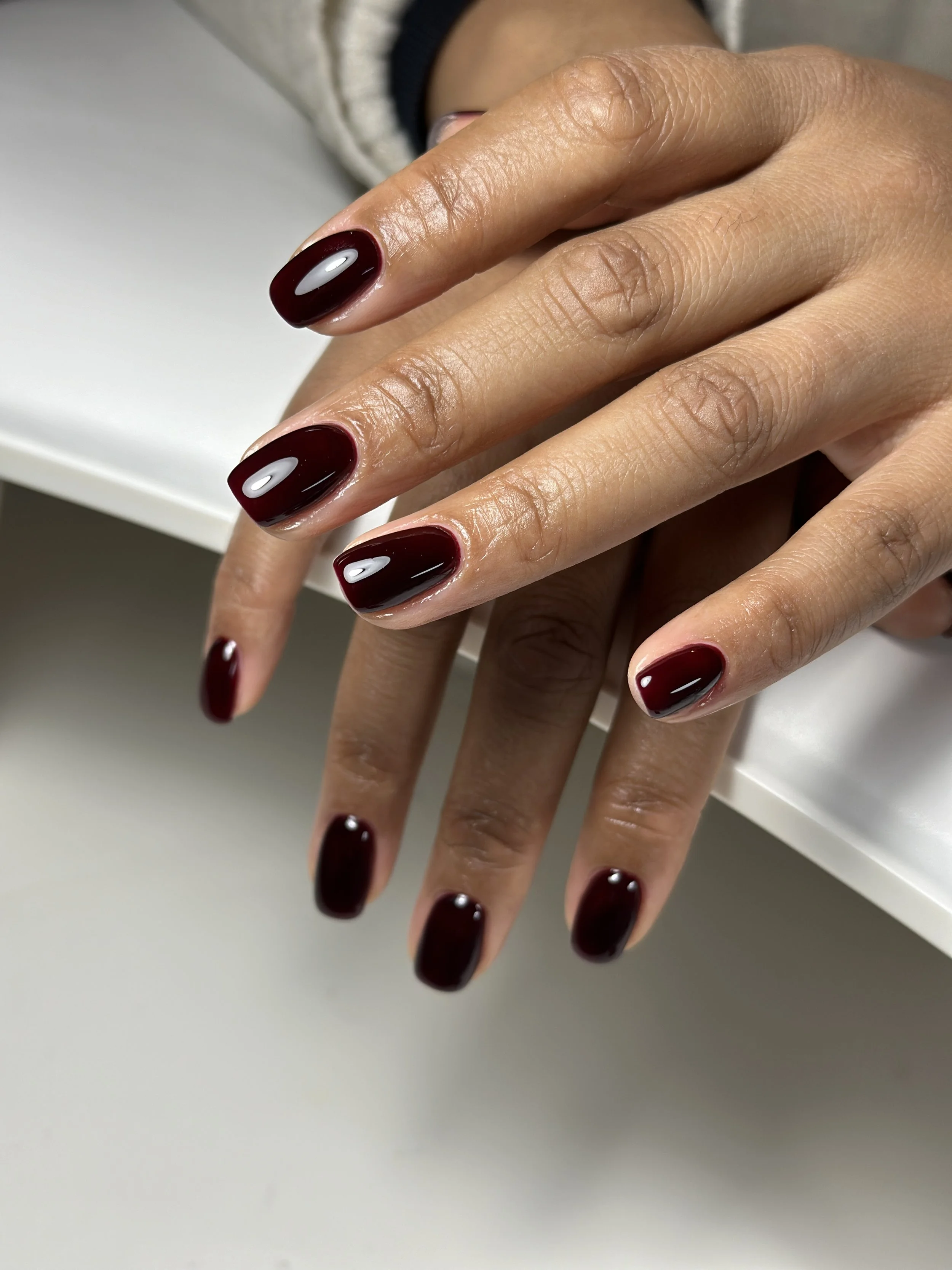 Close-up of hands with nails painted in glossy deep red nail polish.