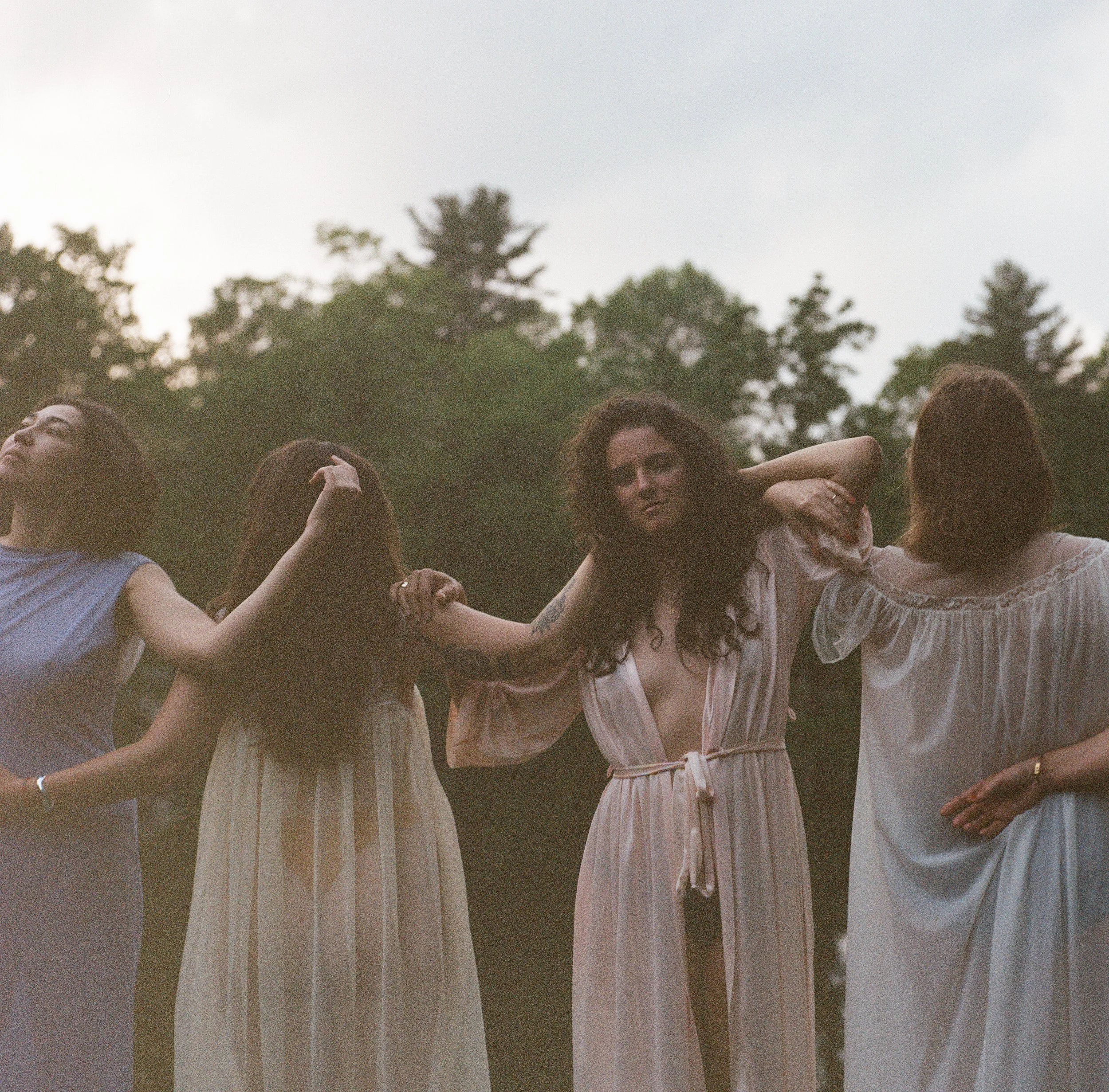 Film photograph of four women in light dresses moving together outdoors at dusk.