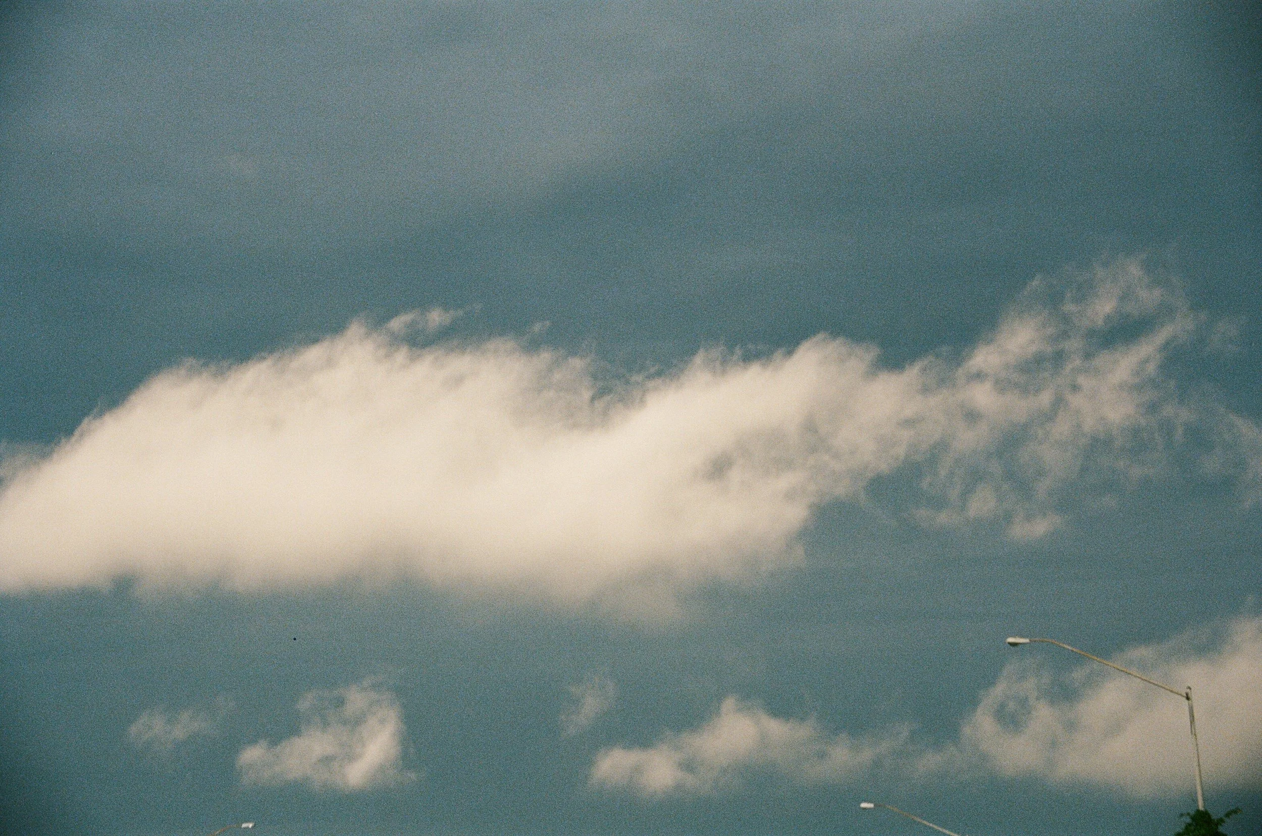 Analog film photograph of a white cloud drifting through a blue sky.