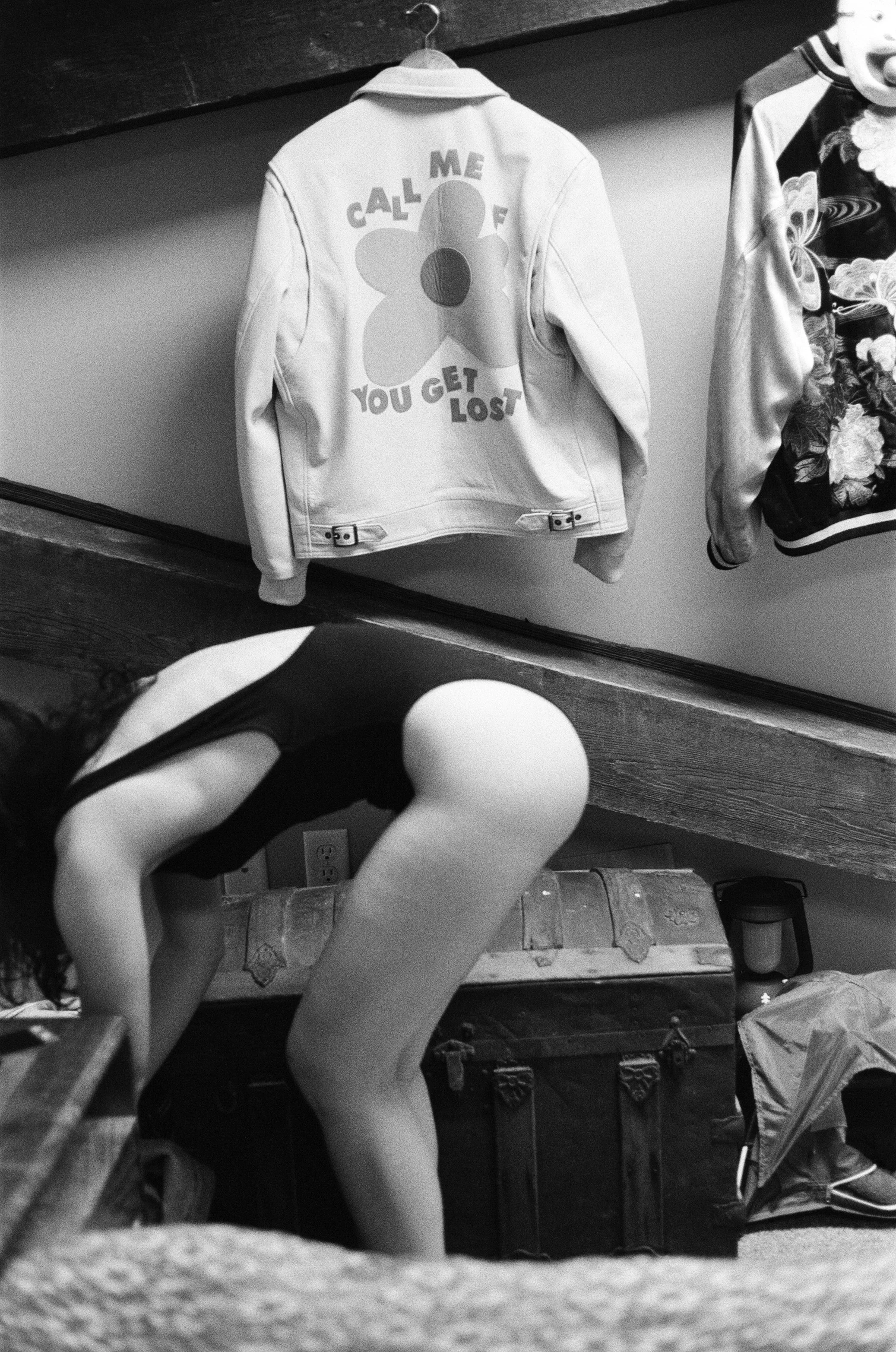 Black-and-white analog film portrait of a woman bending forward in a domestic interior, photographed by Emily Zoe.