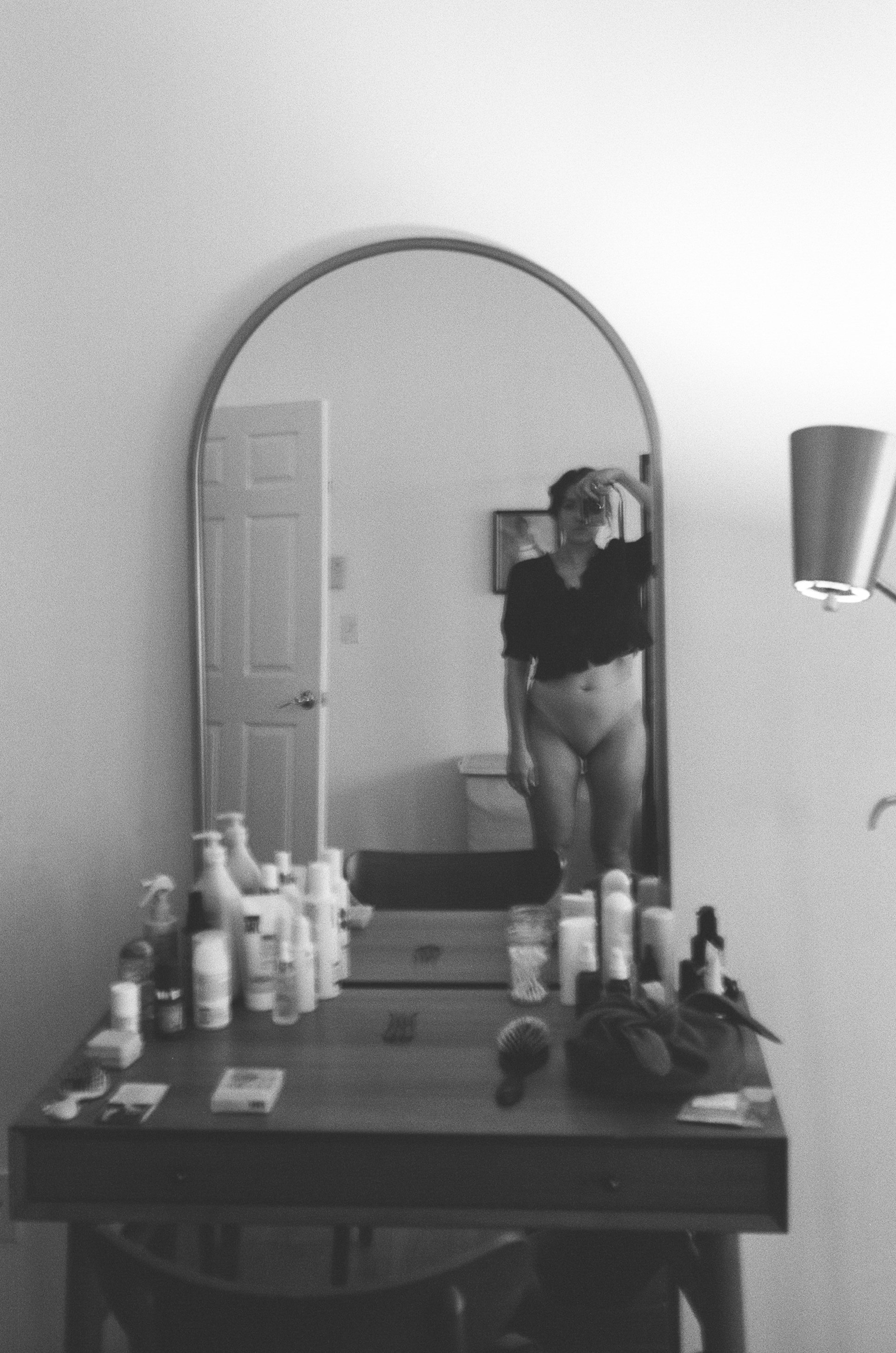 Black-and-white self-portrait of Emily Zōe reflected in an arched mirror.