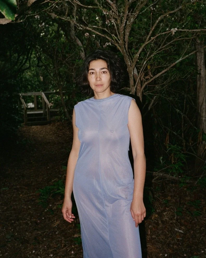 Flash portrait of a woman in a sheer blue dress standing among trees at night.