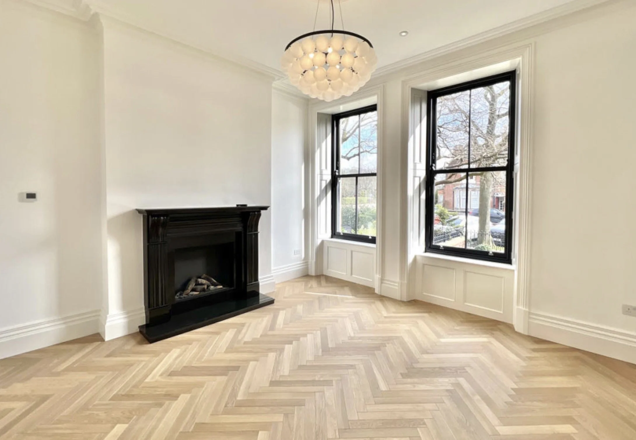 Elegant reception room with herringbone flooring, fireplace and tall sash windows.