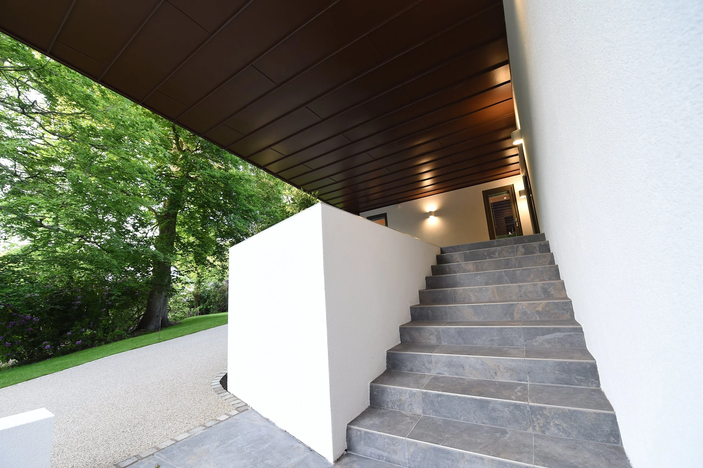 8 Church Drive, Lytham – Steps to Rear Garden Terrace

Architectural photograph showing the stone steps leading to the elevated rear terrace, sheltered beneath the cantilevered first floor with its dark zinc soffit, integrated lighting and views acro