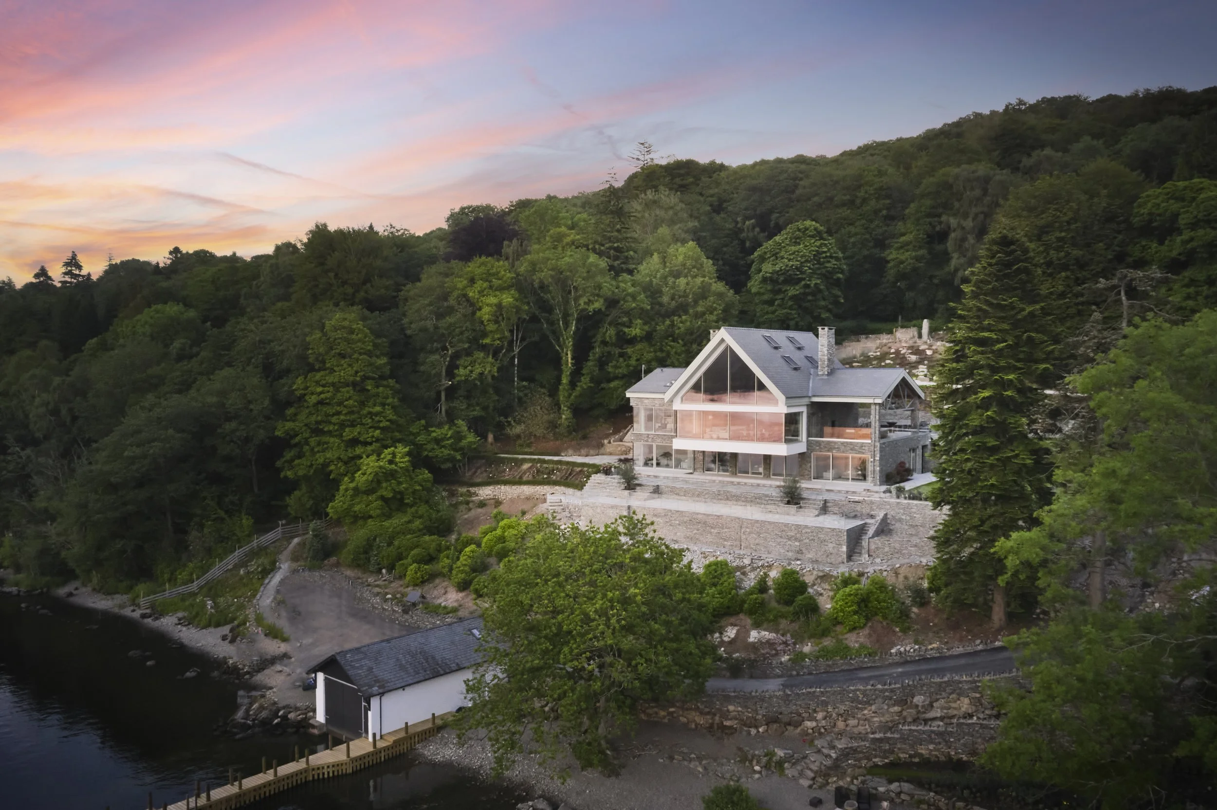 Otter Bank, Lake Windermere — sunset view of the award-winning contemporary lakeside house, set within mature woodland with private boathouse and direct lake frontage.