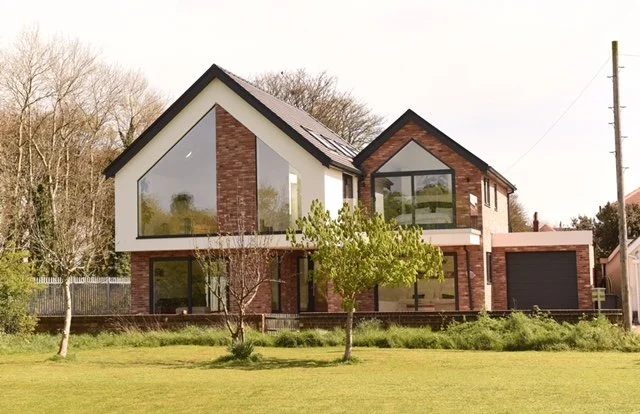 View of St Cuthbert’s Close from Lytham Cricket Ground, a bespoke new-build house in Lytham St Annes designed by Chartered Architect Joel Firth. Contemporary pitched-roof forms, brickwork and large areas of glazing create a modern family home respond