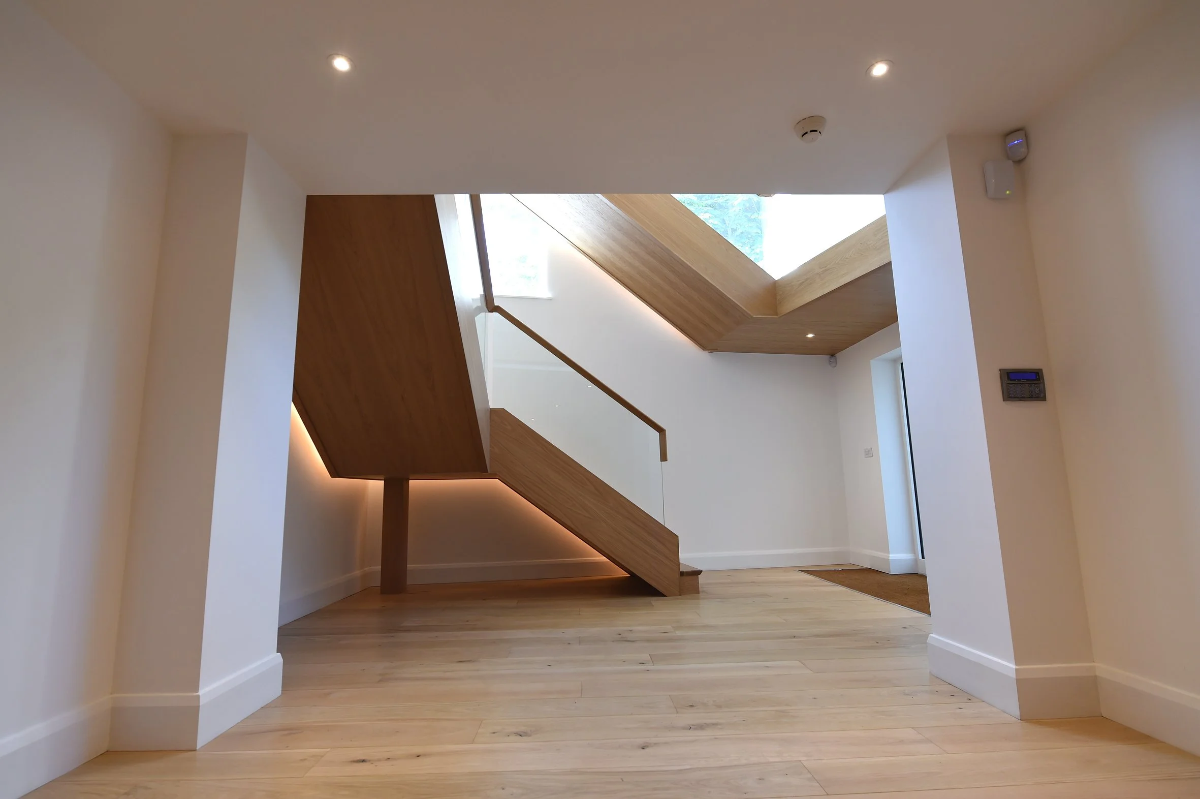 8 Church Drive, Lytham — contemporary entrance hallway featuring a bespoke sculptural timber staircase, oak flooring, concealed LED lighting and a large rooflight bringing natural light into the interior.