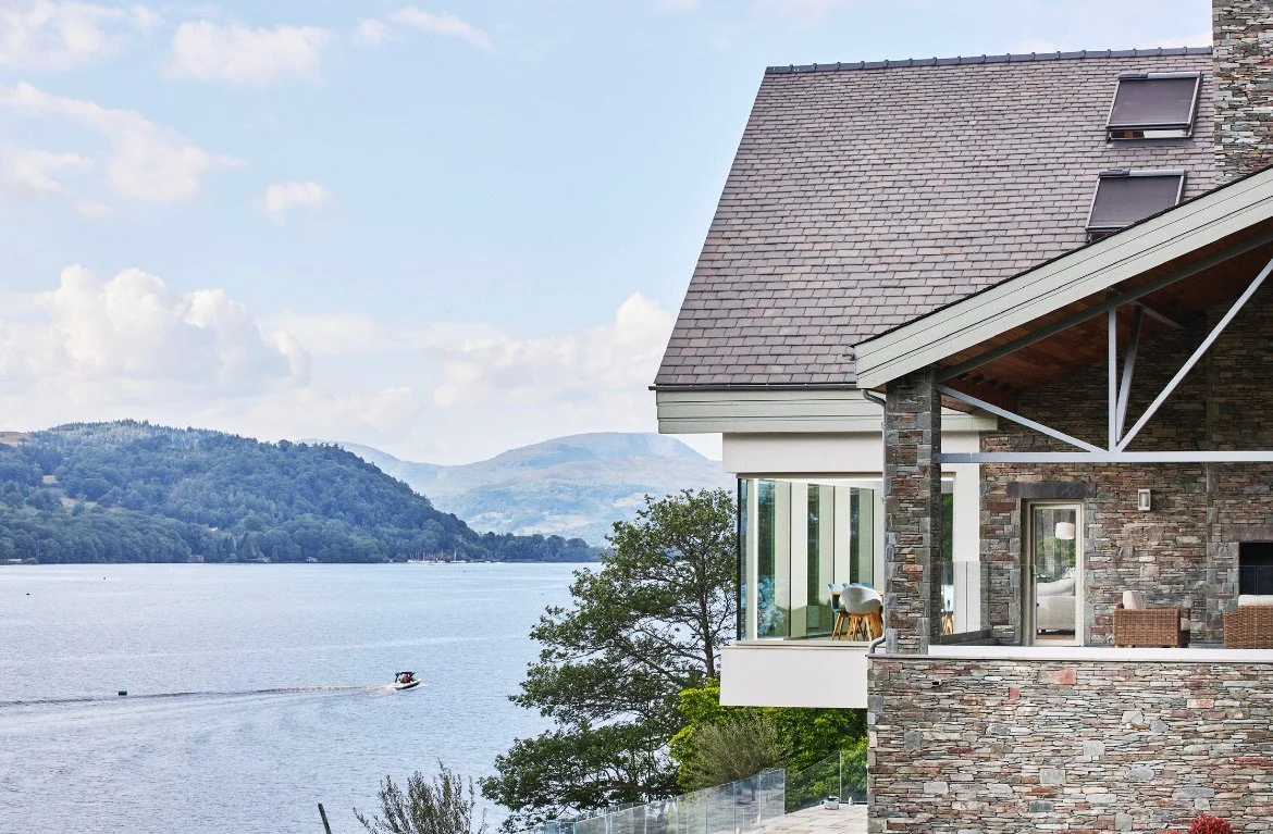 Otter Bank, Lake Windermere — lakeside elevation with natural stone, extensive glazing and framed views across Windermere to the surrounding Lake District fells.