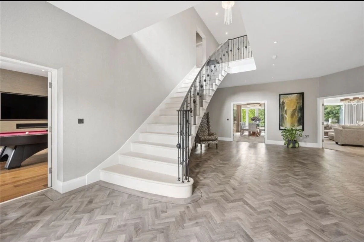 Regent Avenue, Lytham St Annes — Entrance Hall and Staircase Design — spacious contemporary entrance hall featuring an elegant curved staircase with decorative metal balustrades, herringbone flooring and a double-height stairwell. The design combines