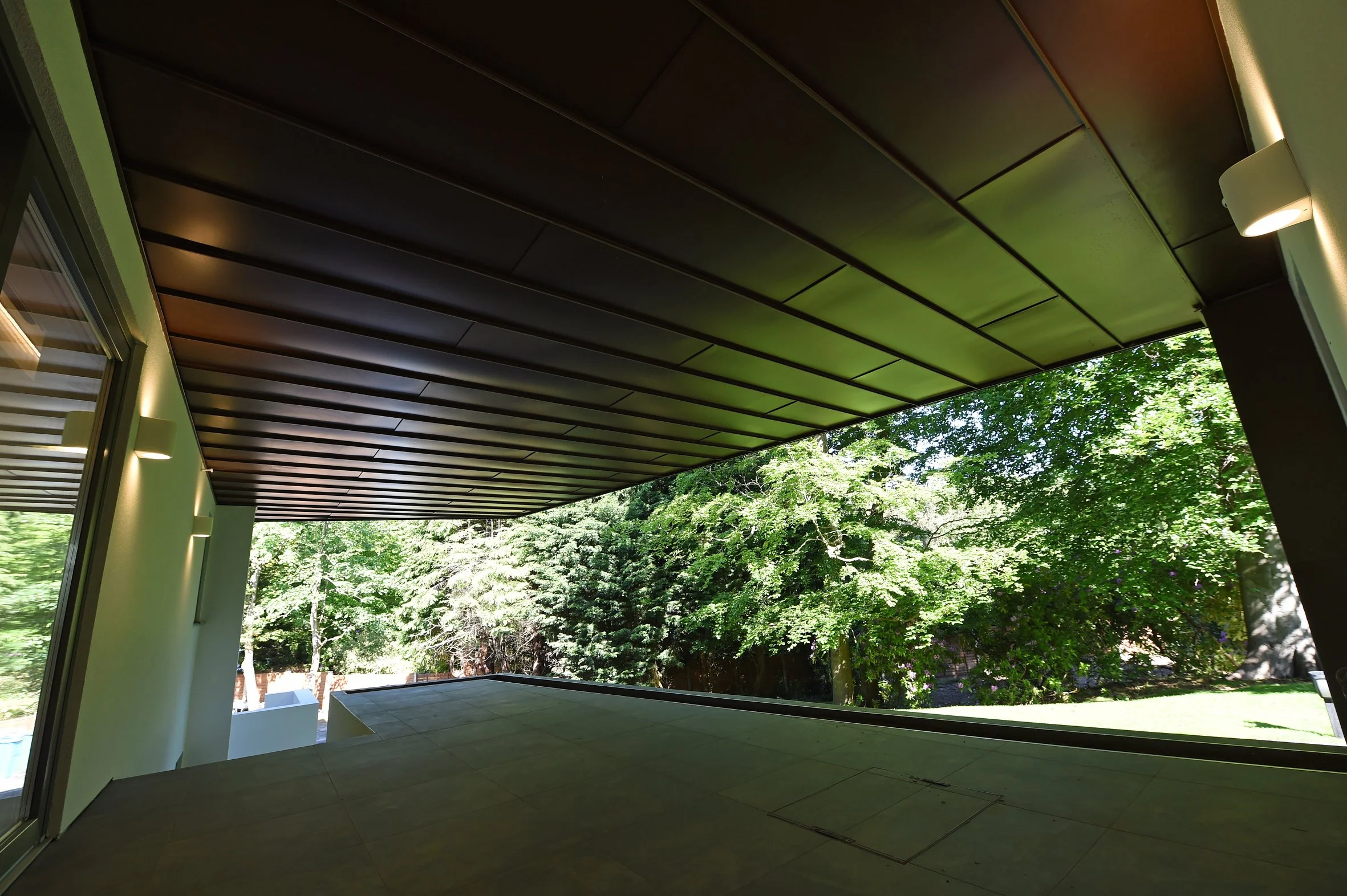 8 Church Drive, Lytham – Cantilevered Rear Terrace

Architectural photograph of the sheltered rear garden terrace adjoining the home office, beneath the dramatic cantilevered first floor with its zinc-clad soffit and views into the landscaped garden.