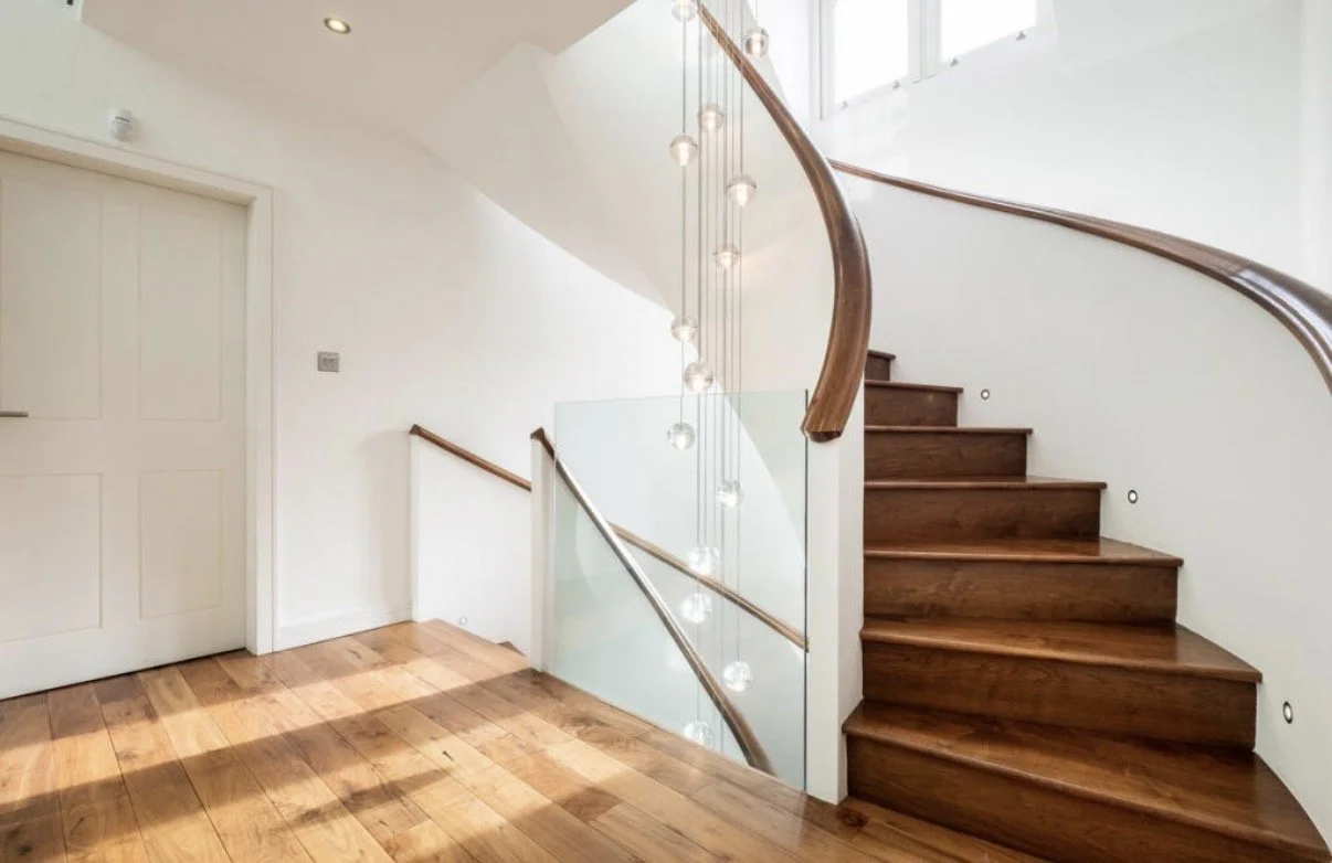 Contemporary curved staircase at Meadowlands, Islay Road, Lytham St Annes, part of the complete refurbishment and remodelling designed by Chartered Architect Joel Firth. Timber treads, a curved timber handrail and frameless glass balustrades create a