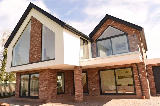 Cricket-ground elevation of St Cuthbert’s Close, Lytham St Annes, a bespoke new-build house designed by Chartered Architect Joel Firth. Contemporary pitched-roof forms, extensive gable glazing and brick detailing frame views towards Lytham Cricket Gr