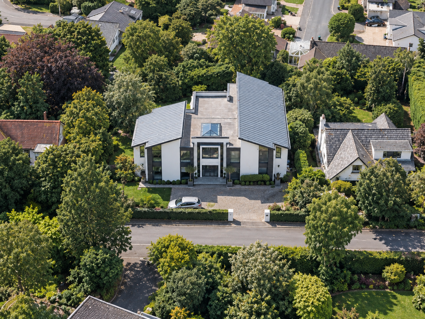 Aerial view of a distinctive contemporary detached home featuring a symmetrical front elevation, central entrance, contrasting architectural materials and mature landscaped surroundings.