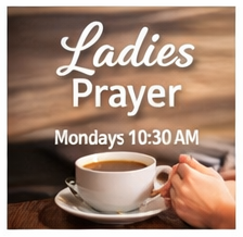Sign reading 'Ladies Prayer, Mondays 10:30 AM' with a cup of coffee and a person holding a spoon in the foreground.