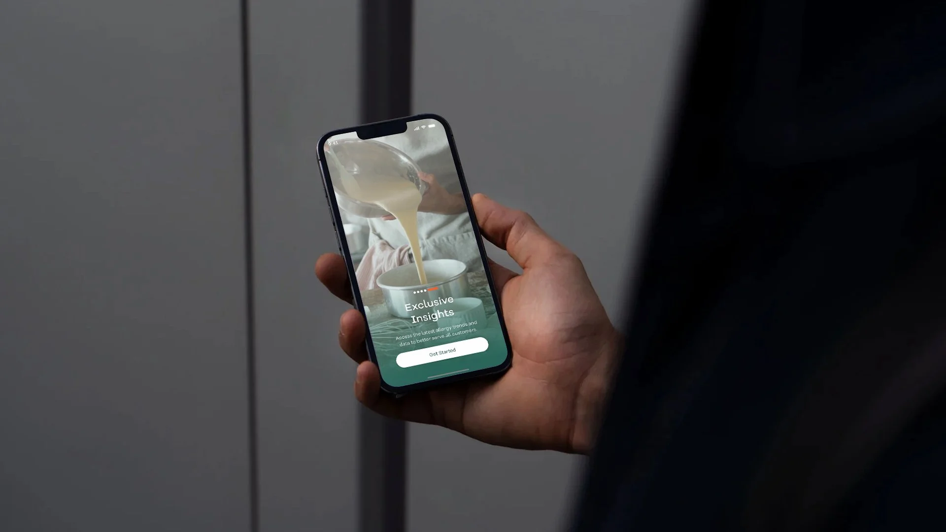 Person holding a smartphone displaying an app with a picture of pouring liquid into a cup and the text "Exclusive Insights" and a "Get Started" button.