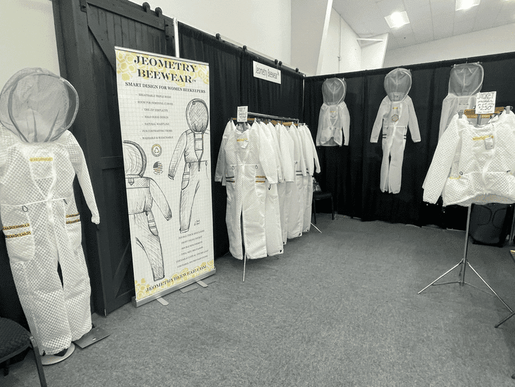 Jeometry™ Beewear booth display featuring Sunny Suits at a beekeeping conference, showcasing women’s beekeeping gear and protective bee suits.