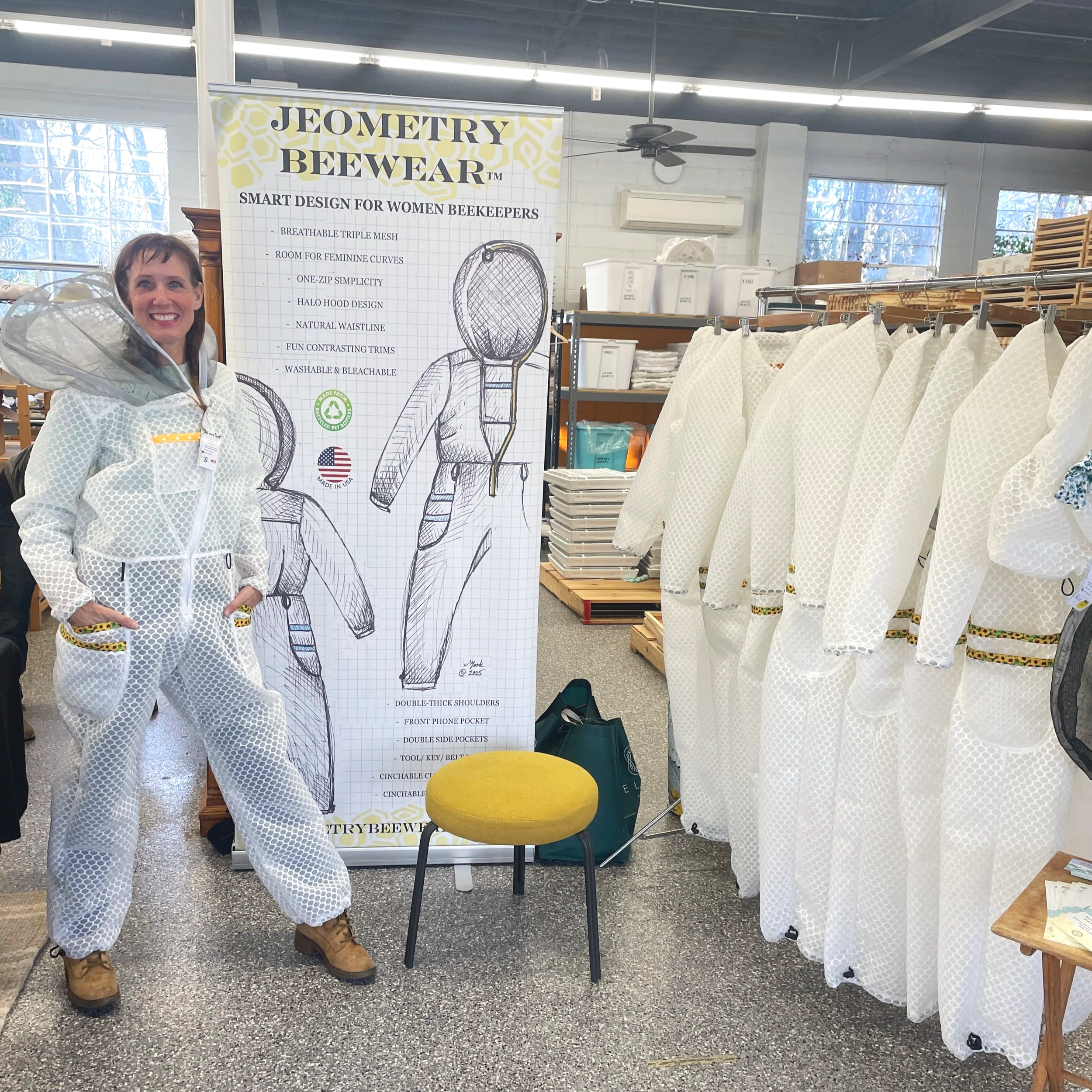 Jenna York standing at the Jeometry Beewear vendor booth at a beekeeping conference wearing her Sunny Suit