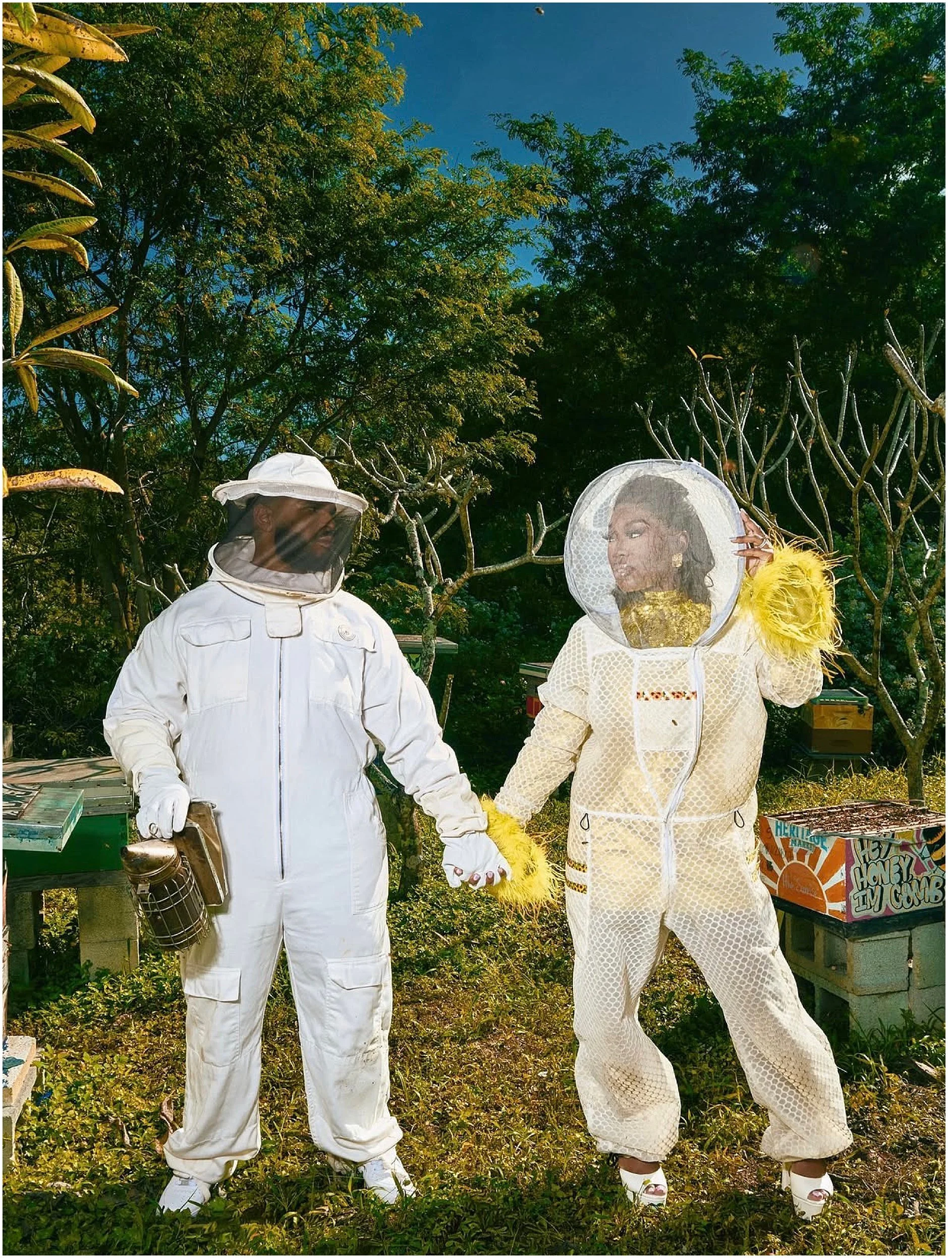 Engagement photo of Erika in the Jeometry Sunny Suit standing beside beehives with her fiancé during a romantic beekeeping-themed session.