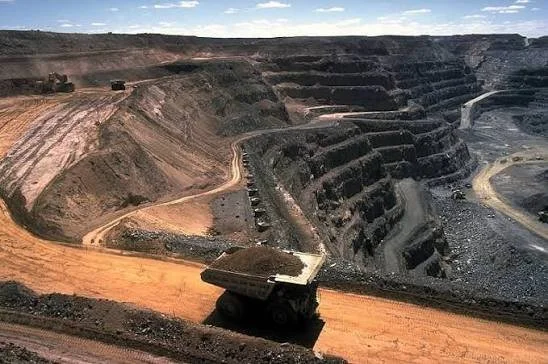 Open-pit mining site with large terraced excavation and a large dump truck on a dirt road