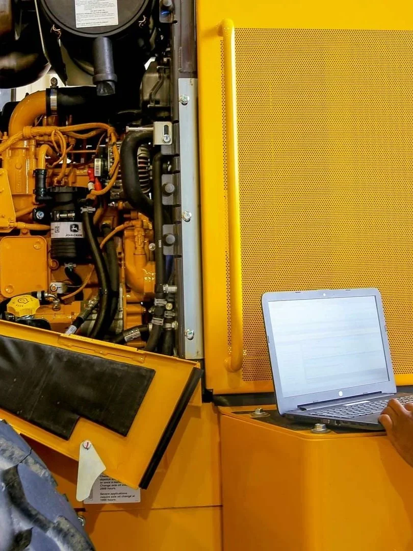 Close-up of a yellow heavy machinery engine with a laptop computer positioned on the side for diagnostics or monitoring.