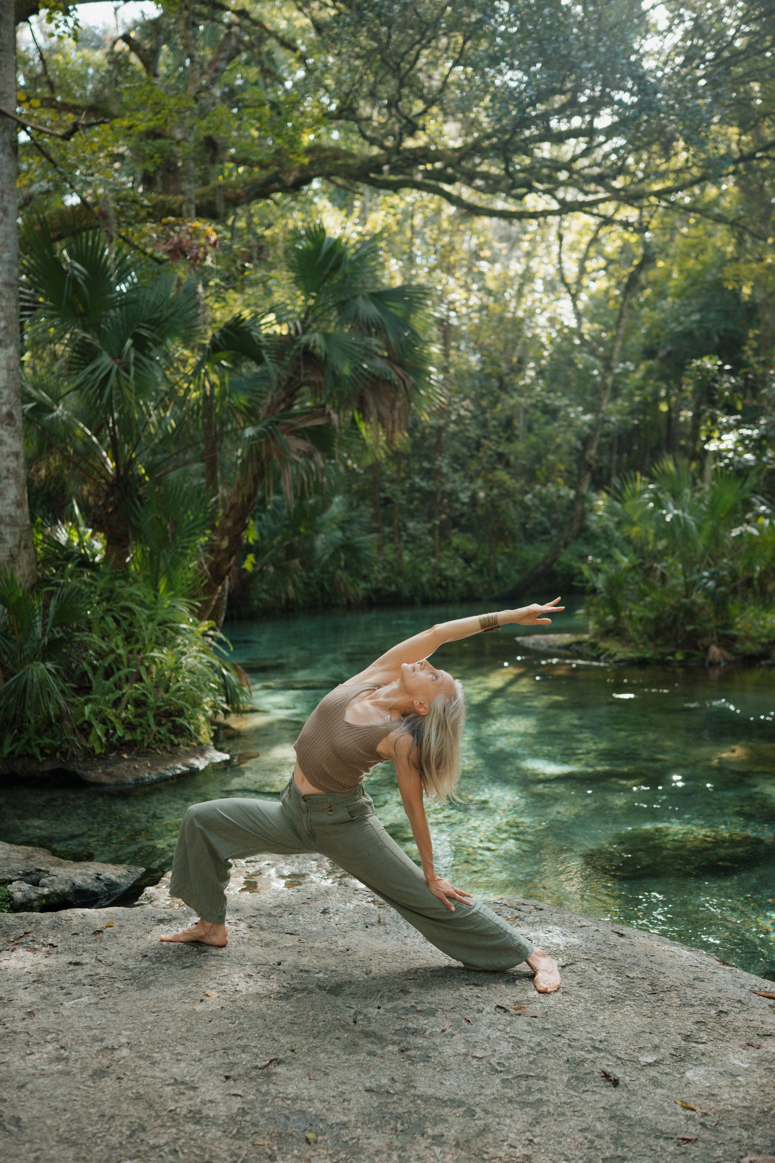 A woman practicing yoga near a river in a lush, green forest during daytime.