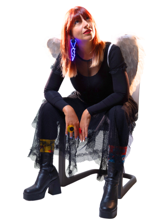 A woman with red hair sitting on a chair, wearing a black dress, large angel wings, and neon-lit blue jewelry of a lightning bolt, with colorful rings on her fingers and black boots.