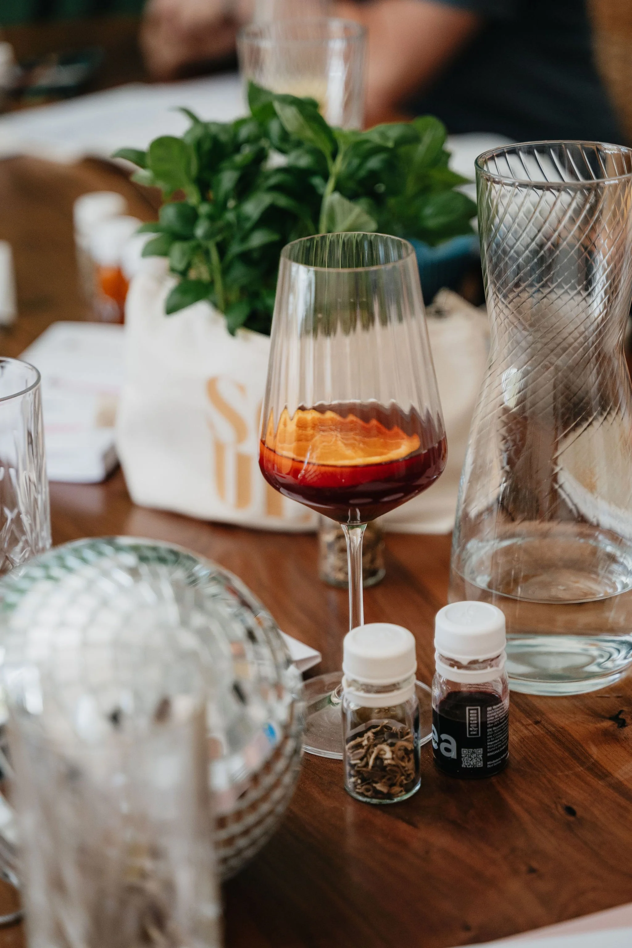 Festlich gedeckter Tisch mit Rotweinglas mit RINGANA Dea, Wassergläsern, grüner Dekoration und Gewürzgläsern.