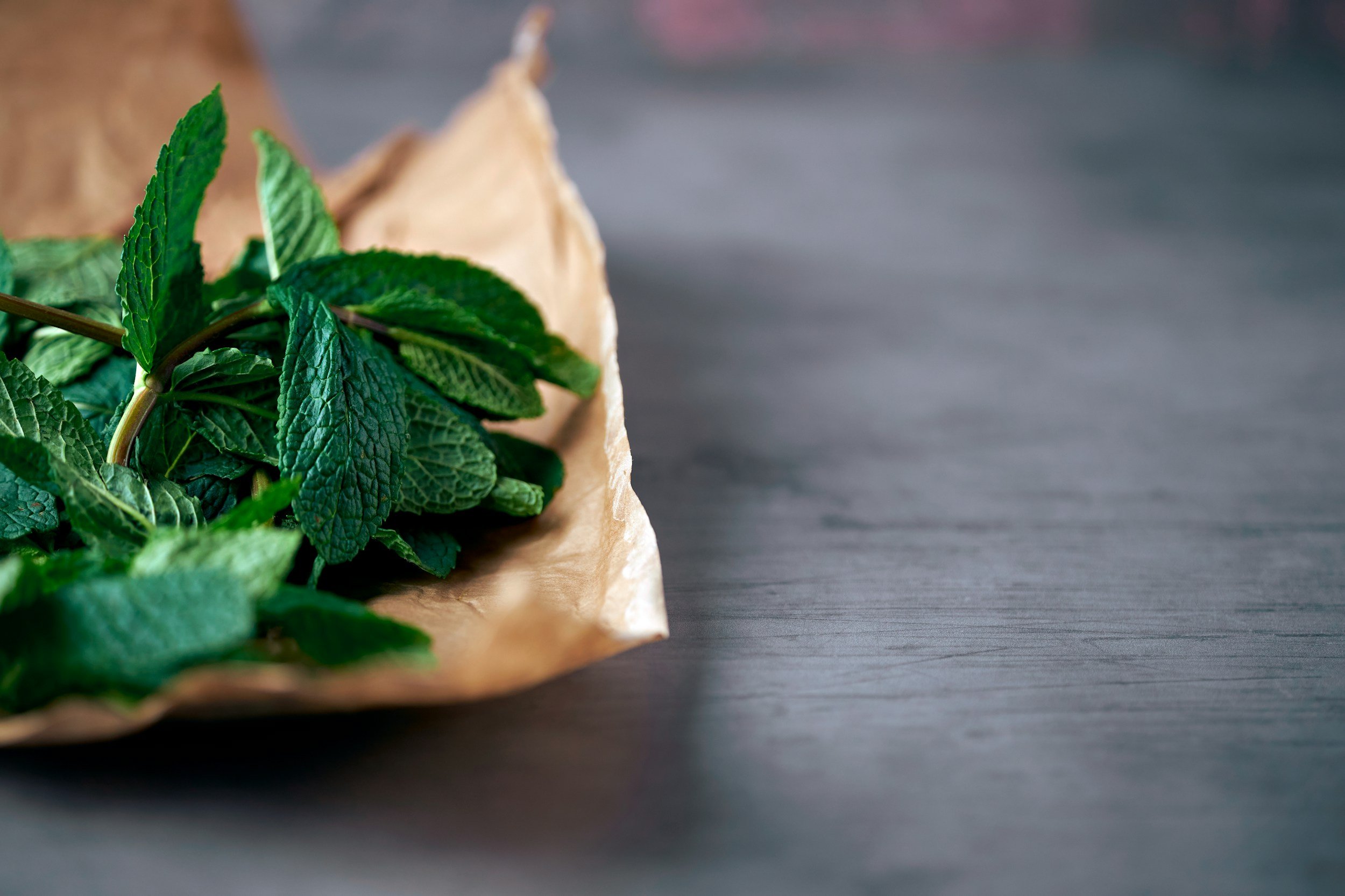 Fresh green mint leaves on brown parchment paper, placed on a dark wooden surface.