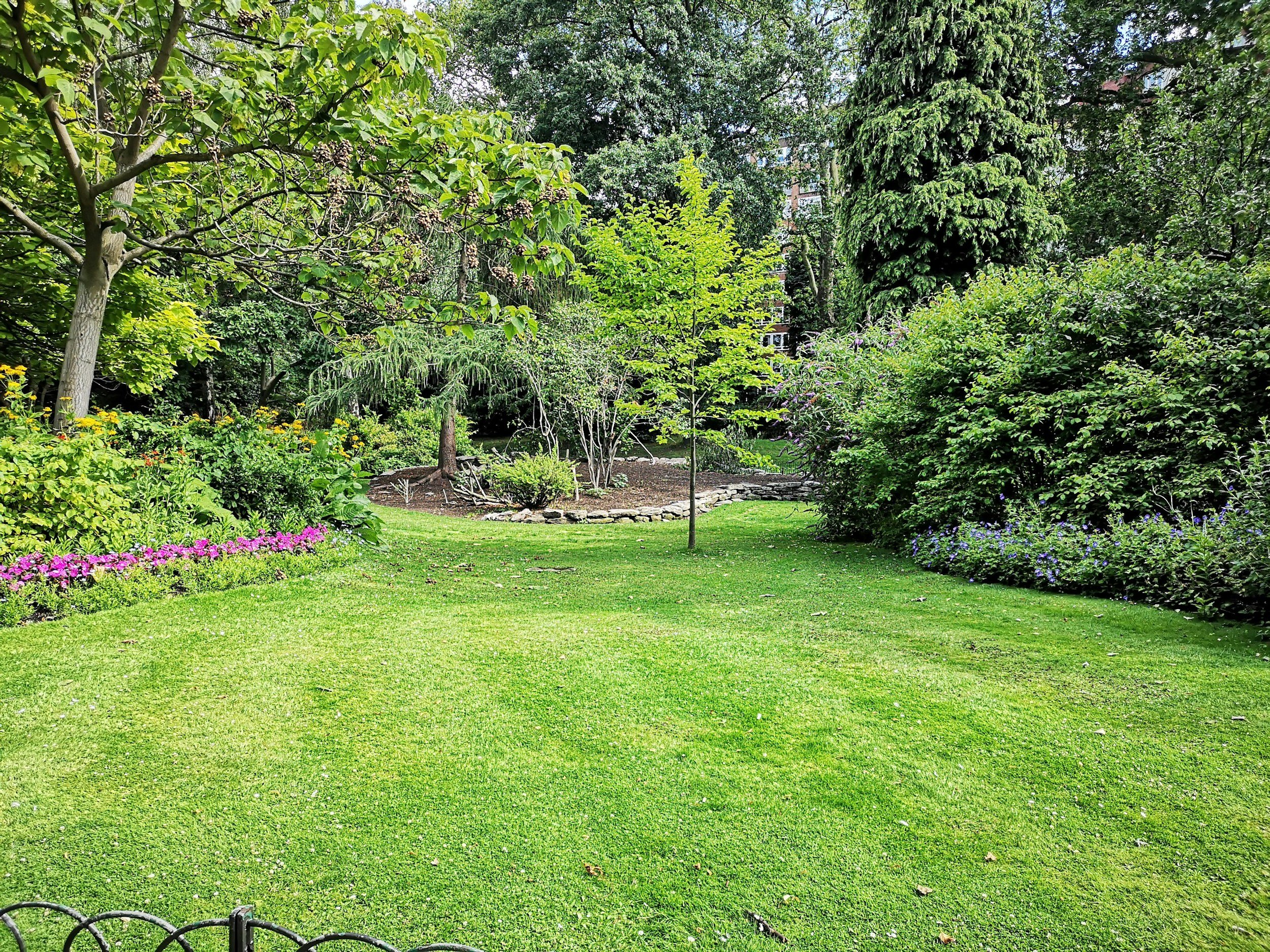 A well-maintained backyard garden with lush green grass, various trees, and flowering plants.