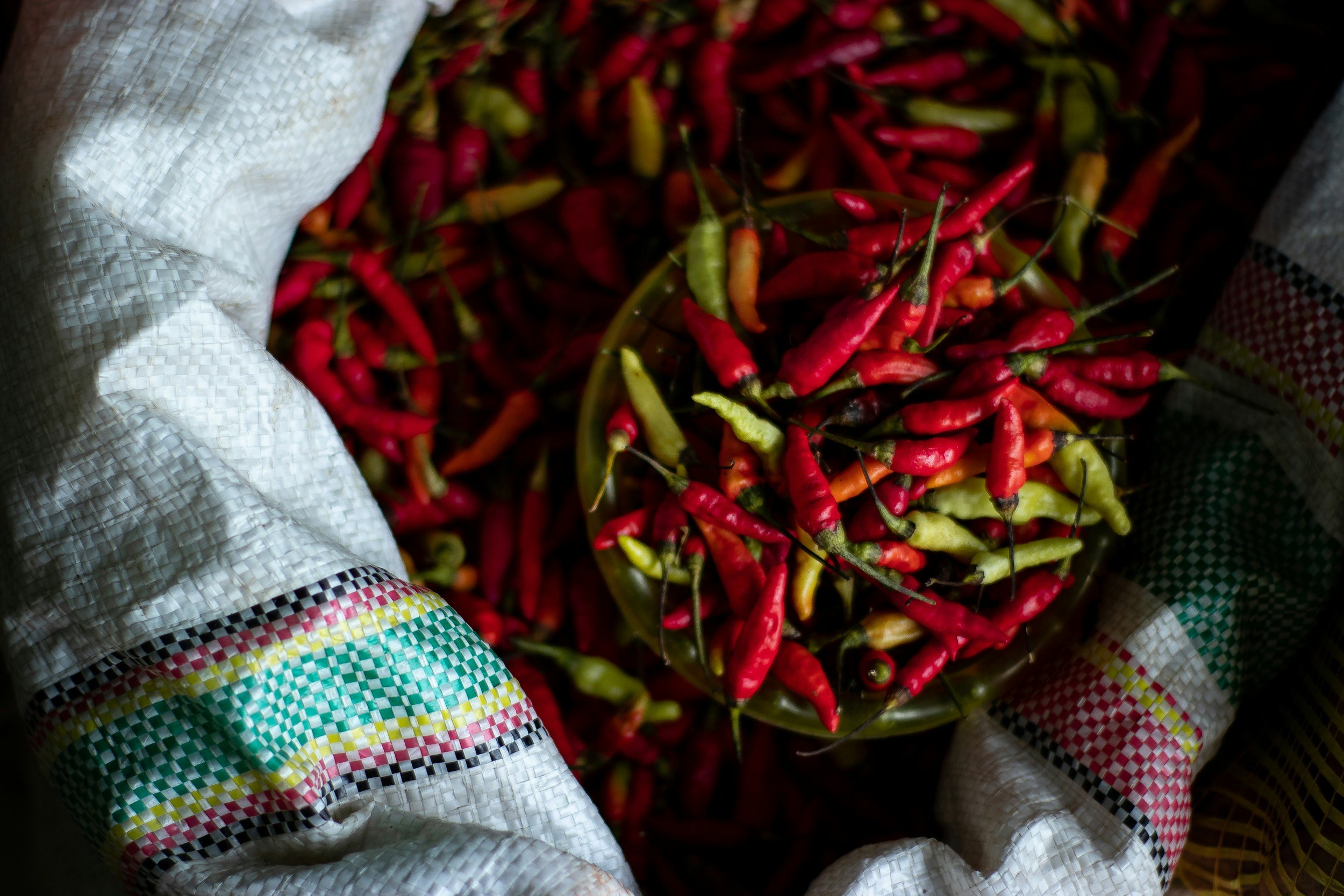 A bowl filled with red, yellow, and green chili peppers surrounded by white fabric with colorful patterns.