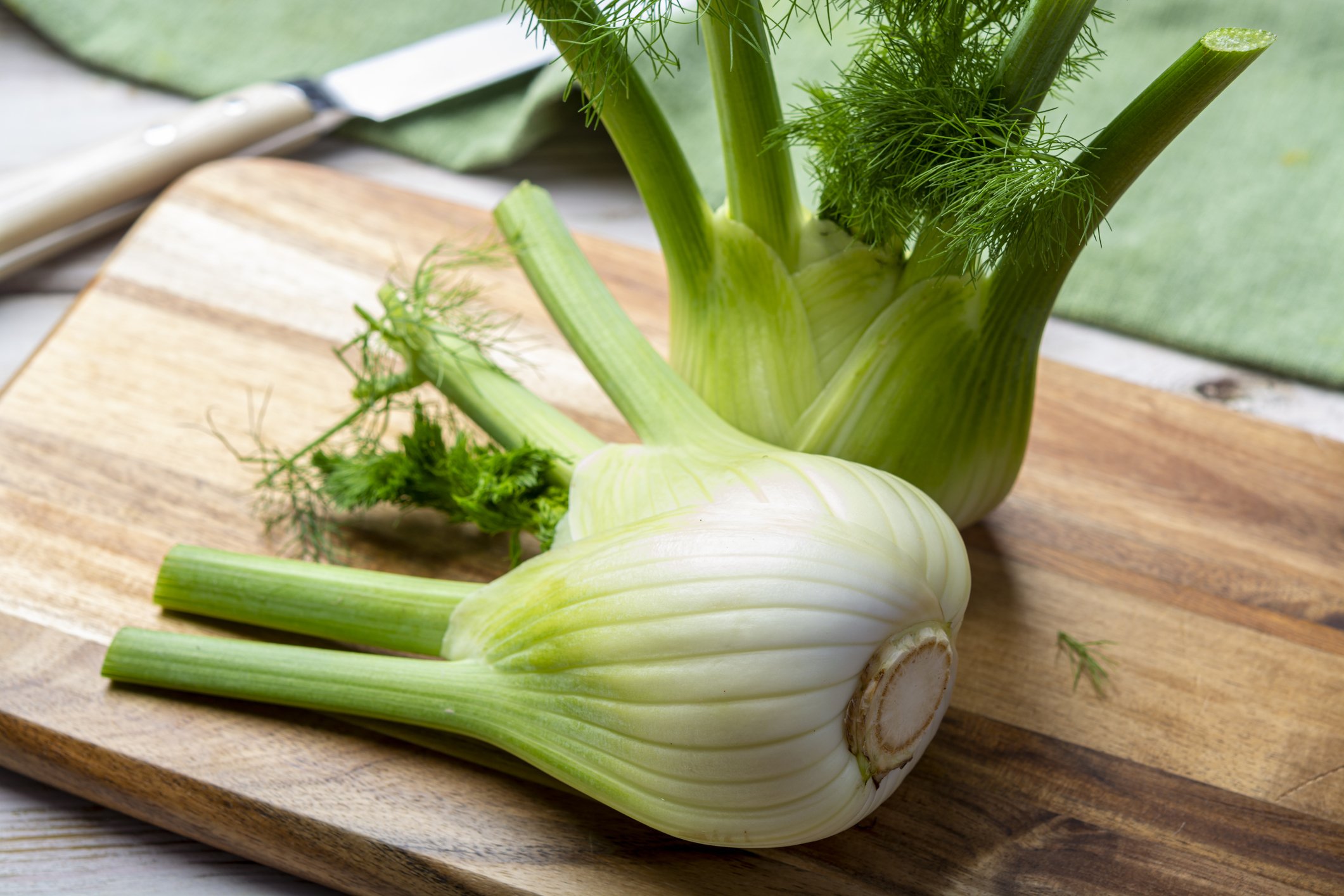 Fennel bulb with green stalks and fronds on a wooden cutting board