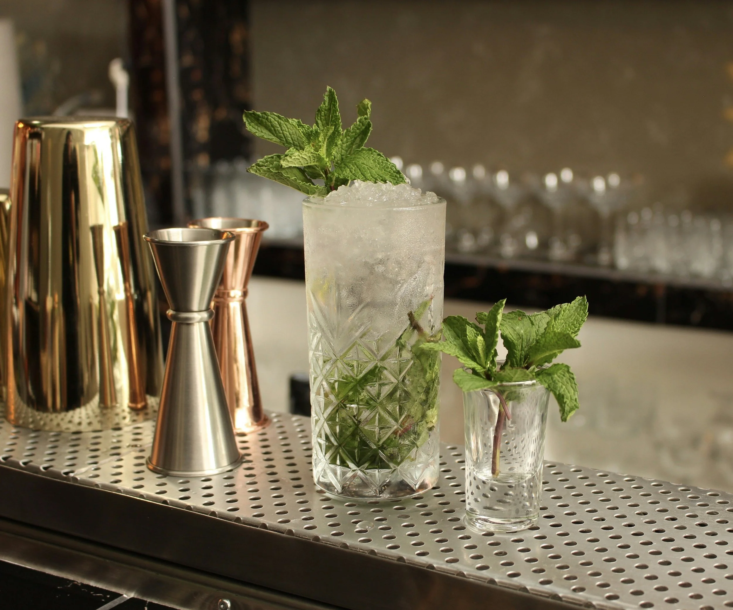 Mojito glass with ice and mint on a vintage bar side with copper cocktail measuring utensils