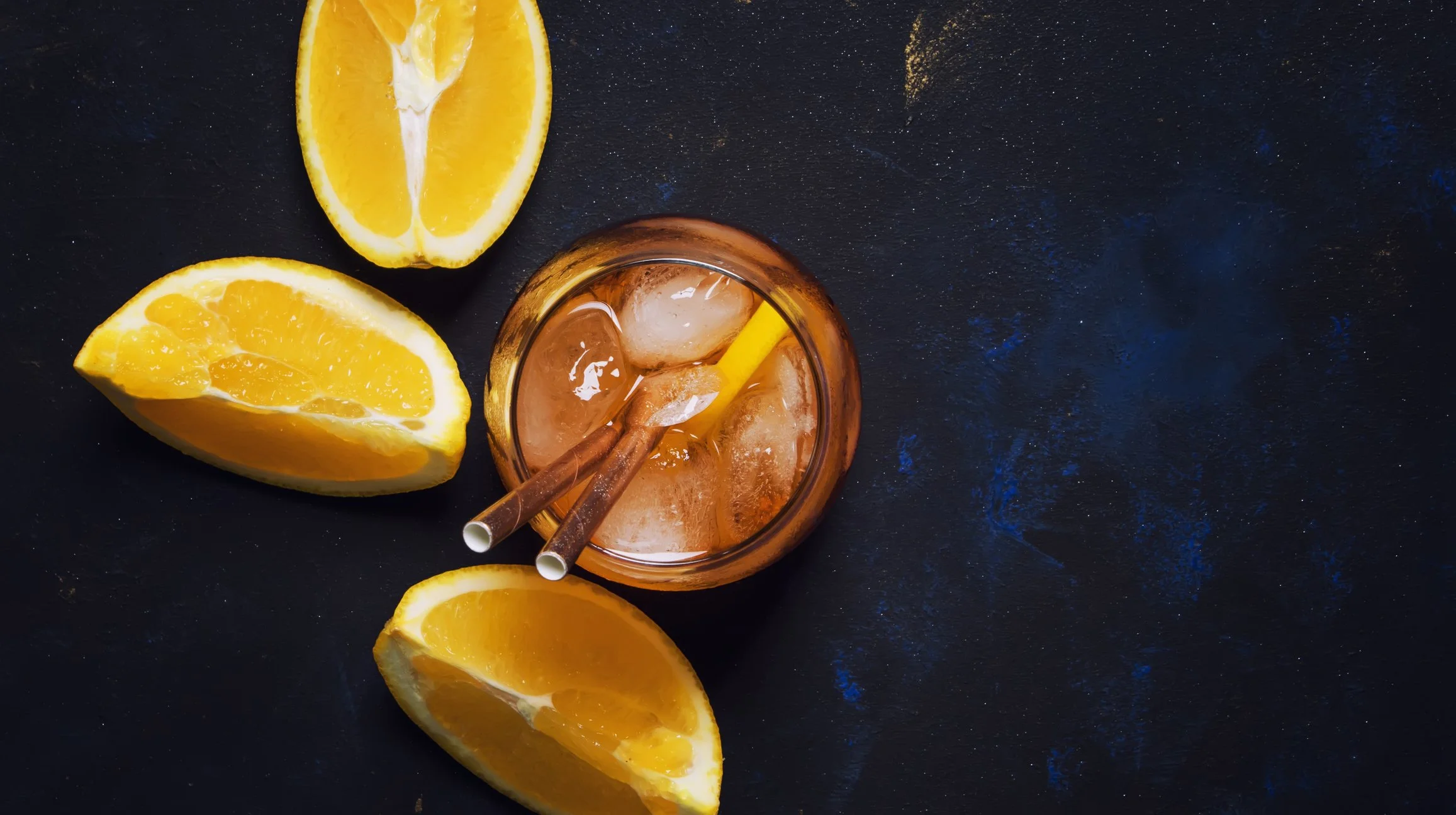 A summer orange citrus spritz drink on a black surface photographed from above with orange slices to garnish
