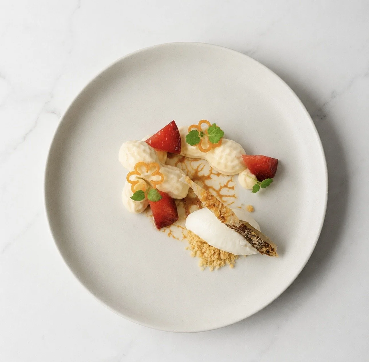 Elegant plated dessert with strawberries, cream, edible flowers, and garnishes on a white plate.