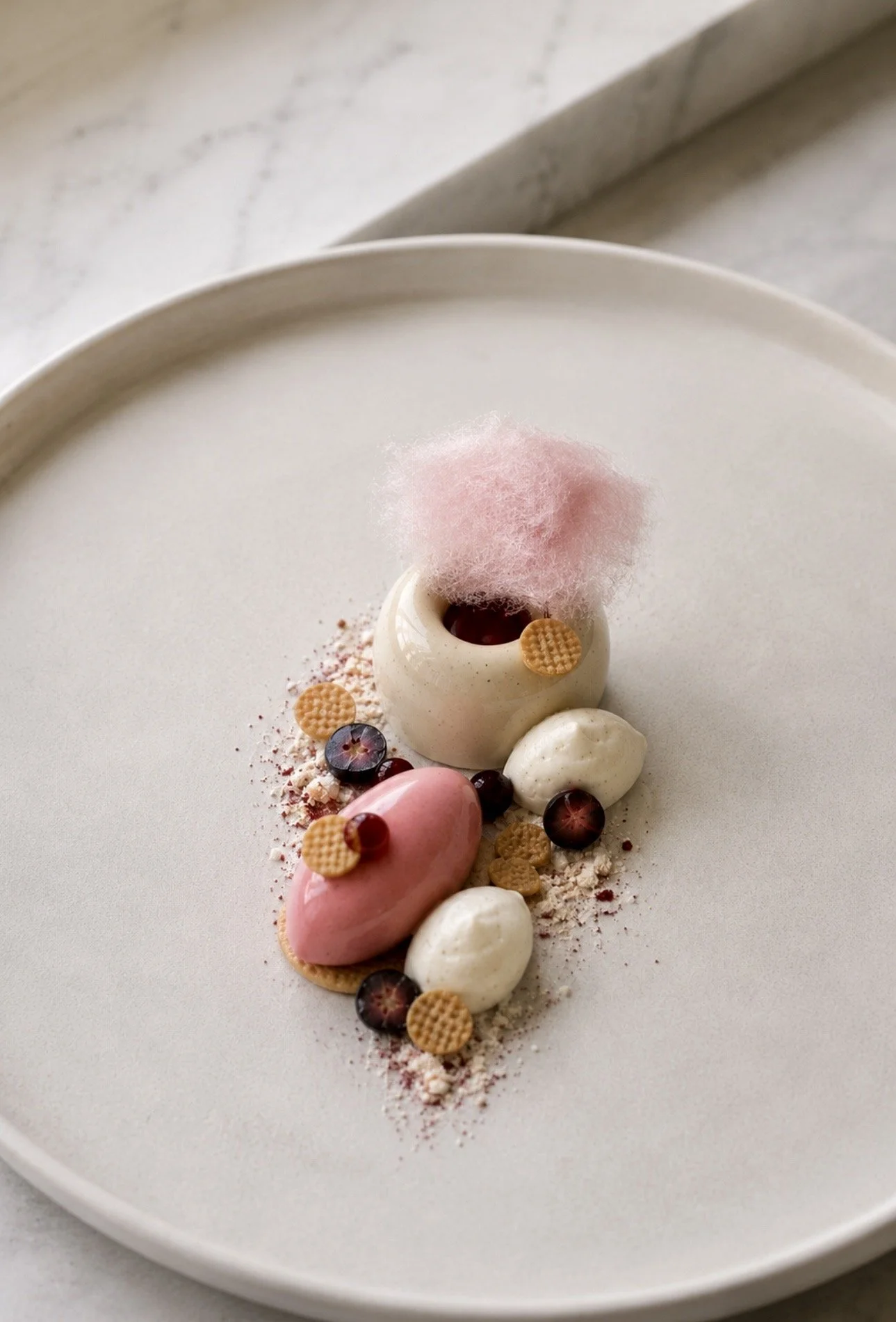 A dessert presentation on a white plate with various small confections, berries, and pink cotton candy.
