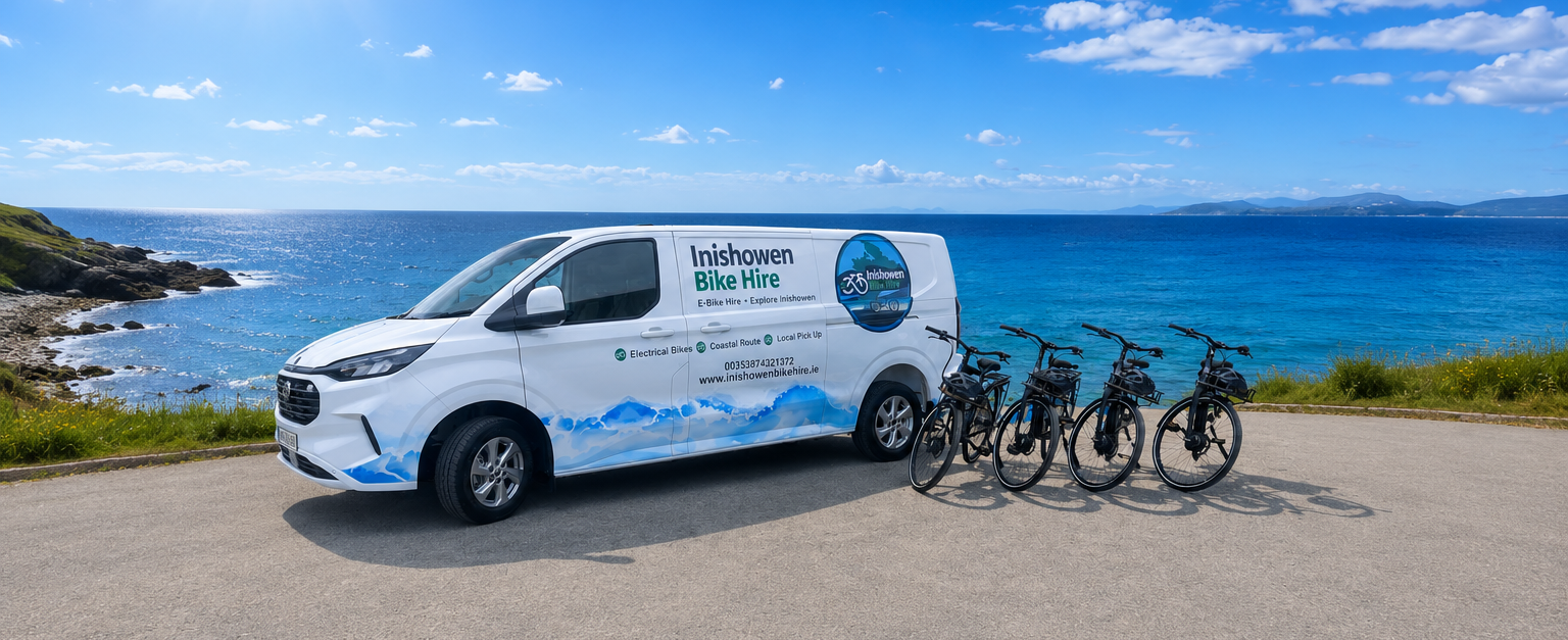 A white van with the words "Inishowen Bike Hire" and a logo parked on a paved area beside four electric bikes. The background features a scenic view of the ocean and blue sky with a few clouds.