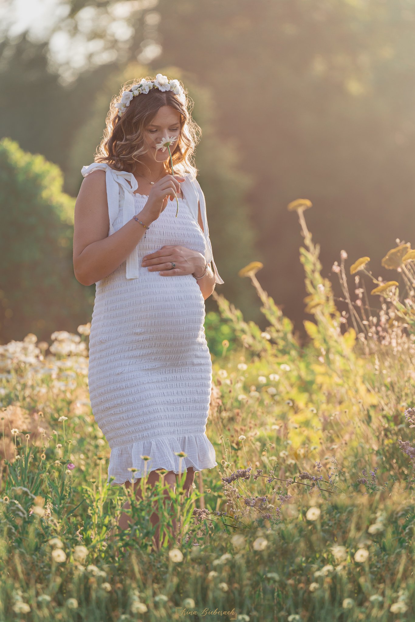 Femme blonde enceinte sent une fleur pendant un coucher de soleil dans le parc de l île Saint Germain