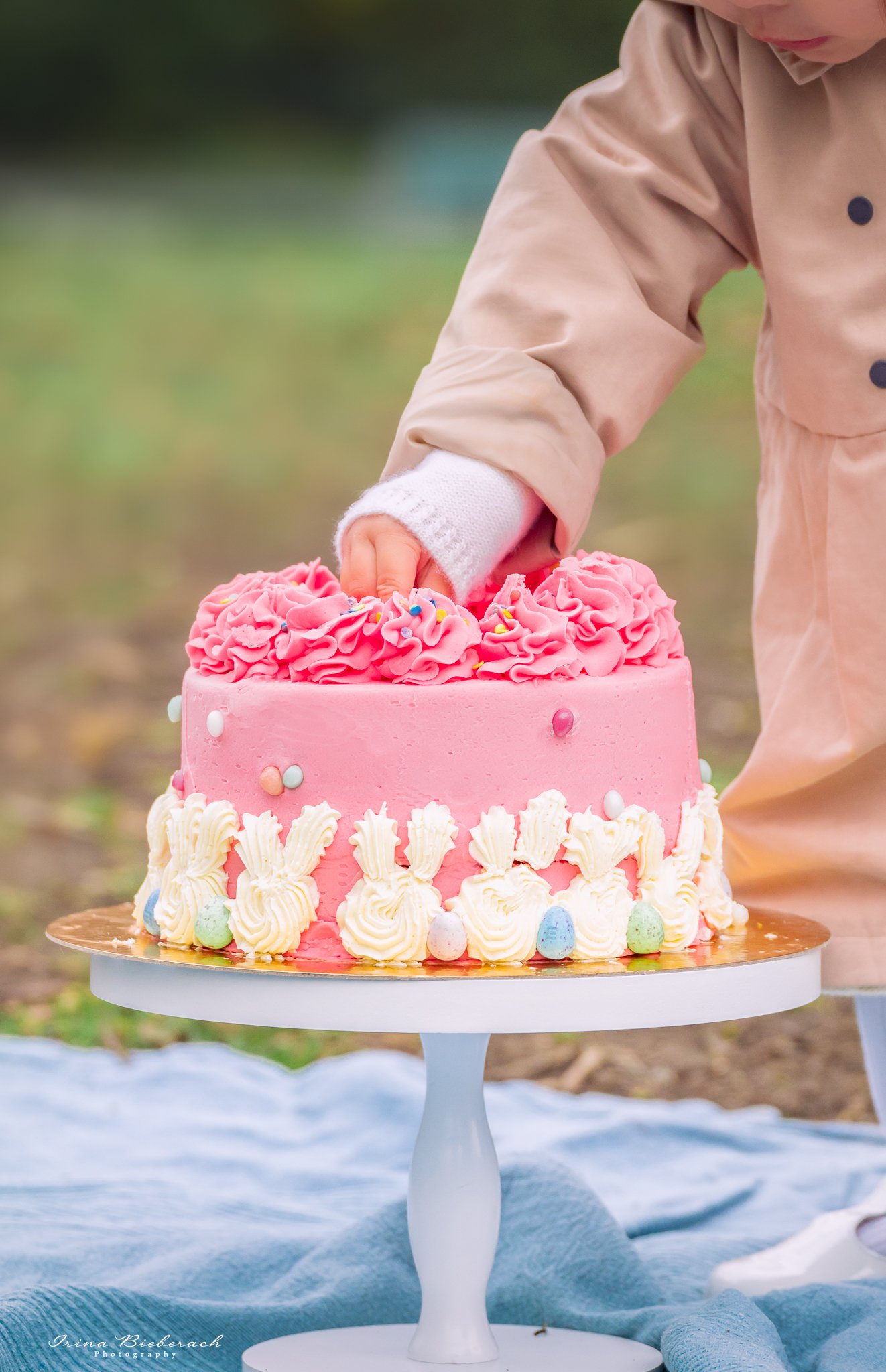 Gâteau d'anniversaire rose sur support blanc en bois et une main d'enfant qui plonge sur le décor du gâteau 