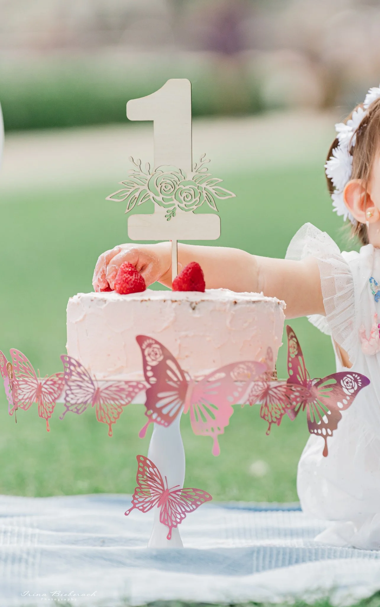 Gateau d'anniversaire rose avec fraisesavec topper chiffre un et main d'une bébé qui prend une fraise