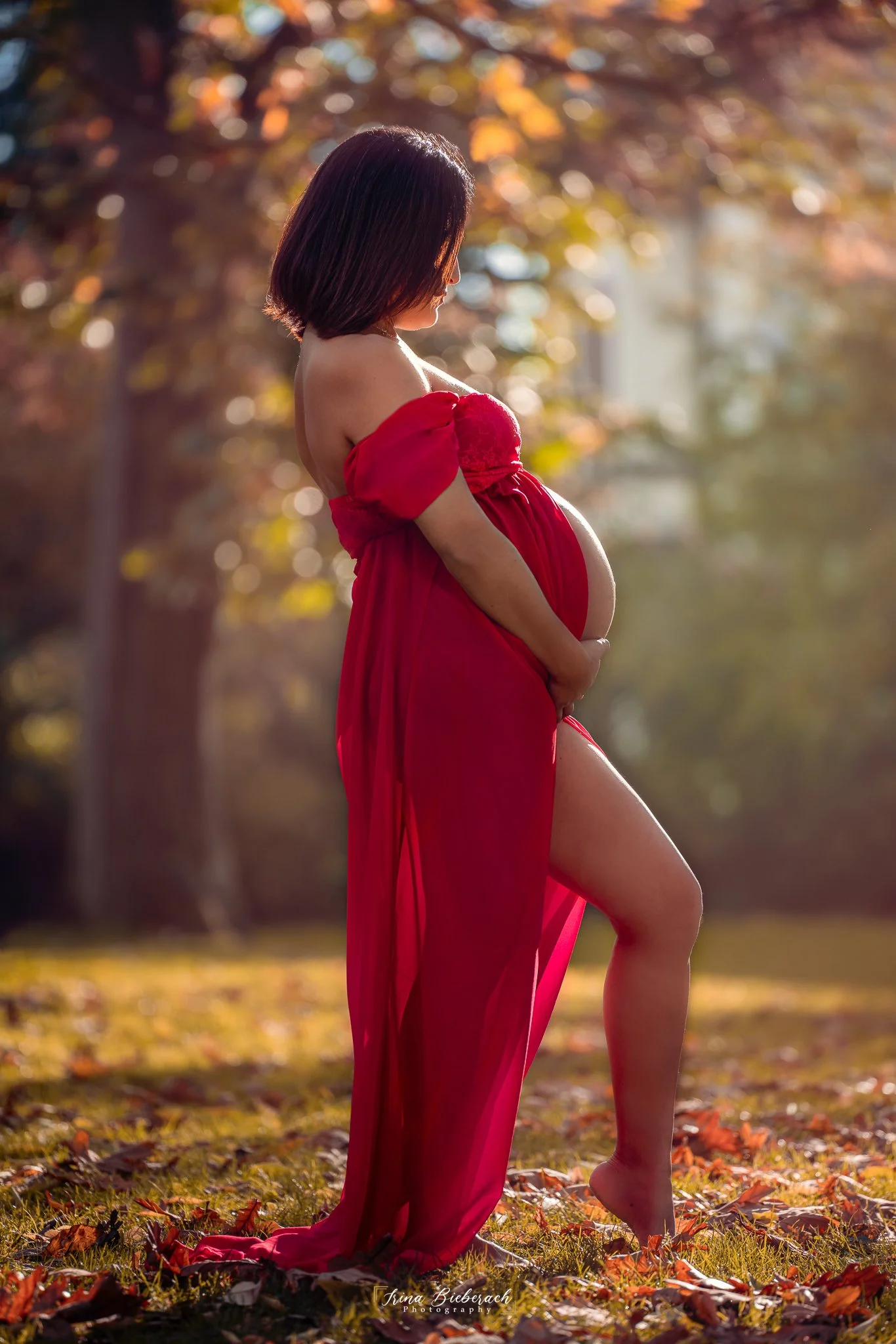 Femme enceinte pose en robe rouge pendant un coucher de soleil dans le parc Montsouris de Paris
