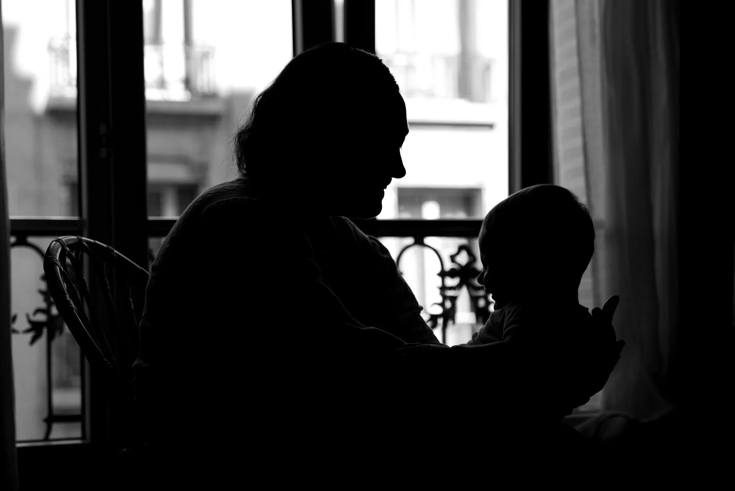 Silhouette d'une femme assise qui porte un bébé en contre jour devant une fenêtre d’appariement