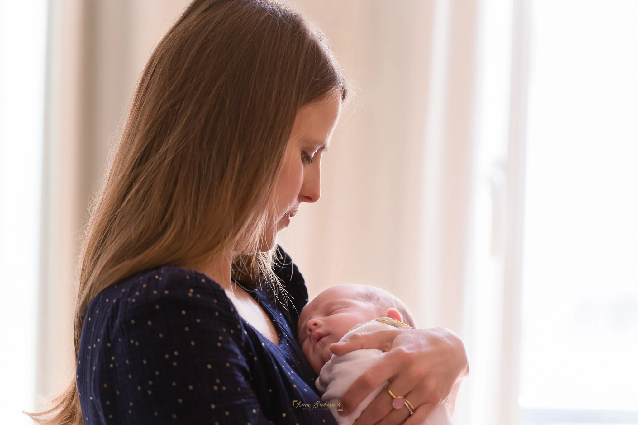 Jeune maman porte son bébé fille éclairées par la lumière qui rentre par la fenêtre 