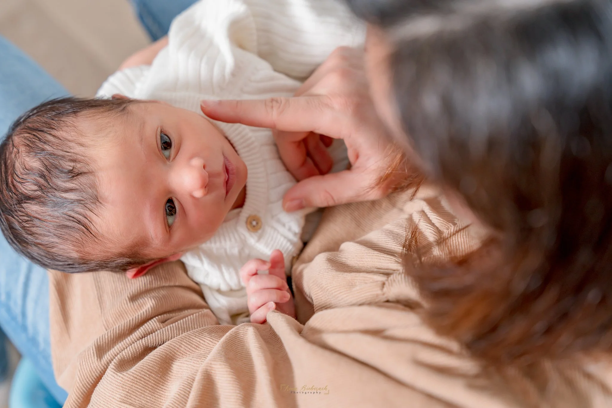 Une main touche tendrement le visage d'un nourrisson qui regarde sa maman