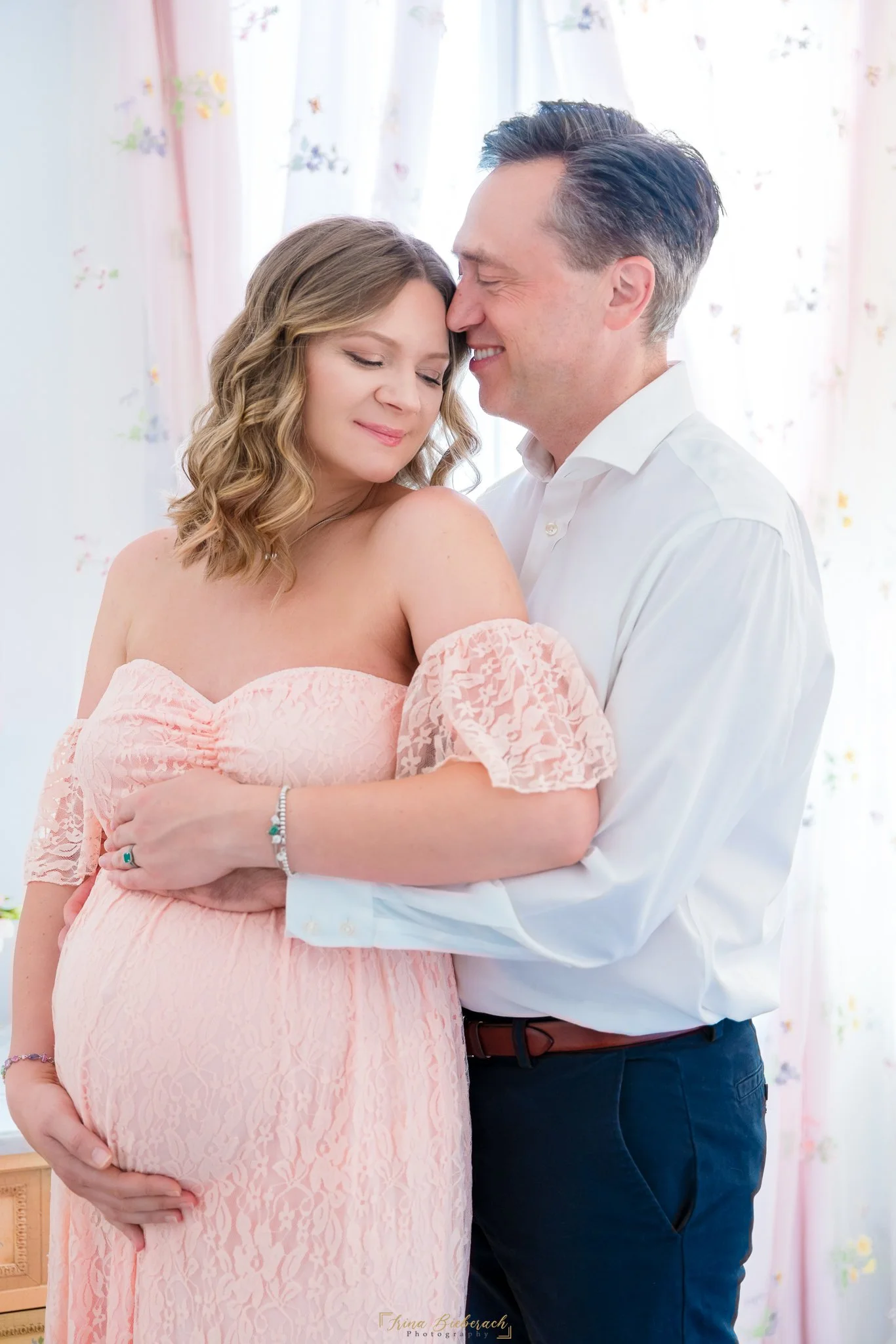 Homme embrasse son épouse enceinte habillée en rose 