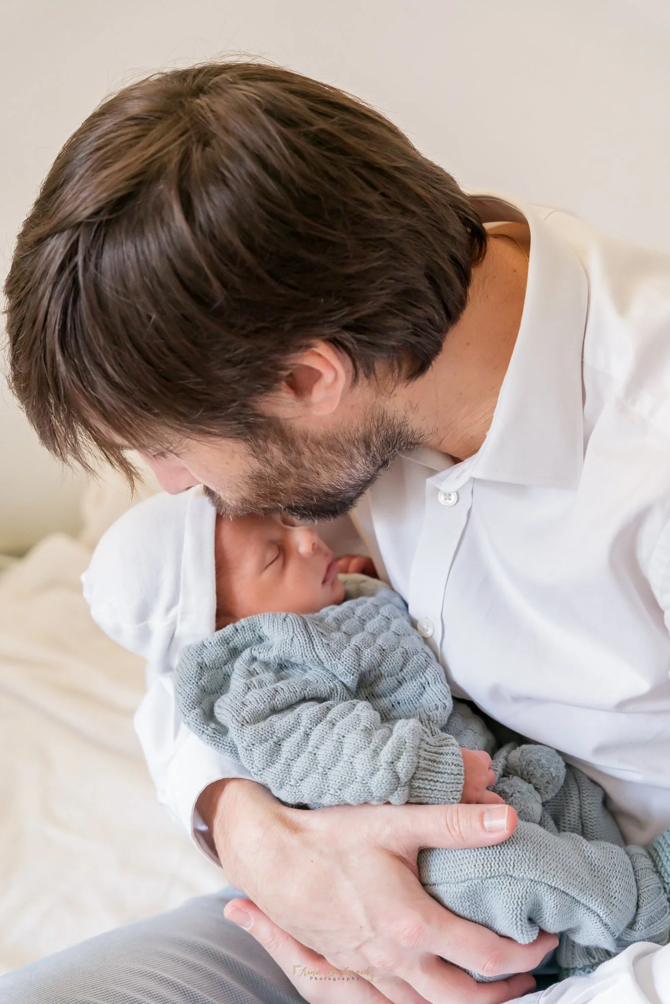 Jeune père embrasse sur le front son fils nouveau né qui dort dans ses bras