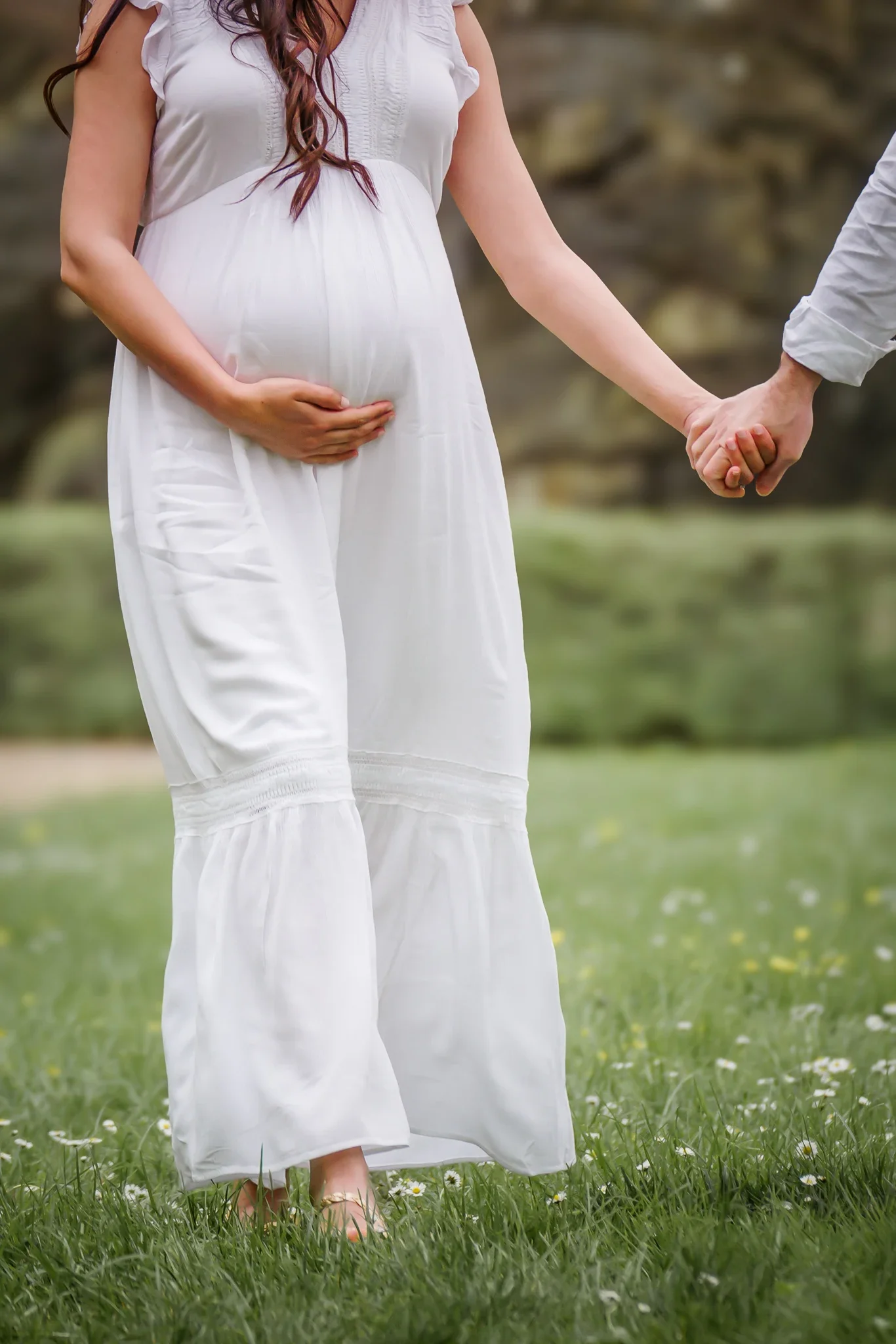 Couple se tient les mains en marchant au Parc de Sceaux pendant la floraison des cerisiers blancs pour une séance photo de grossesse